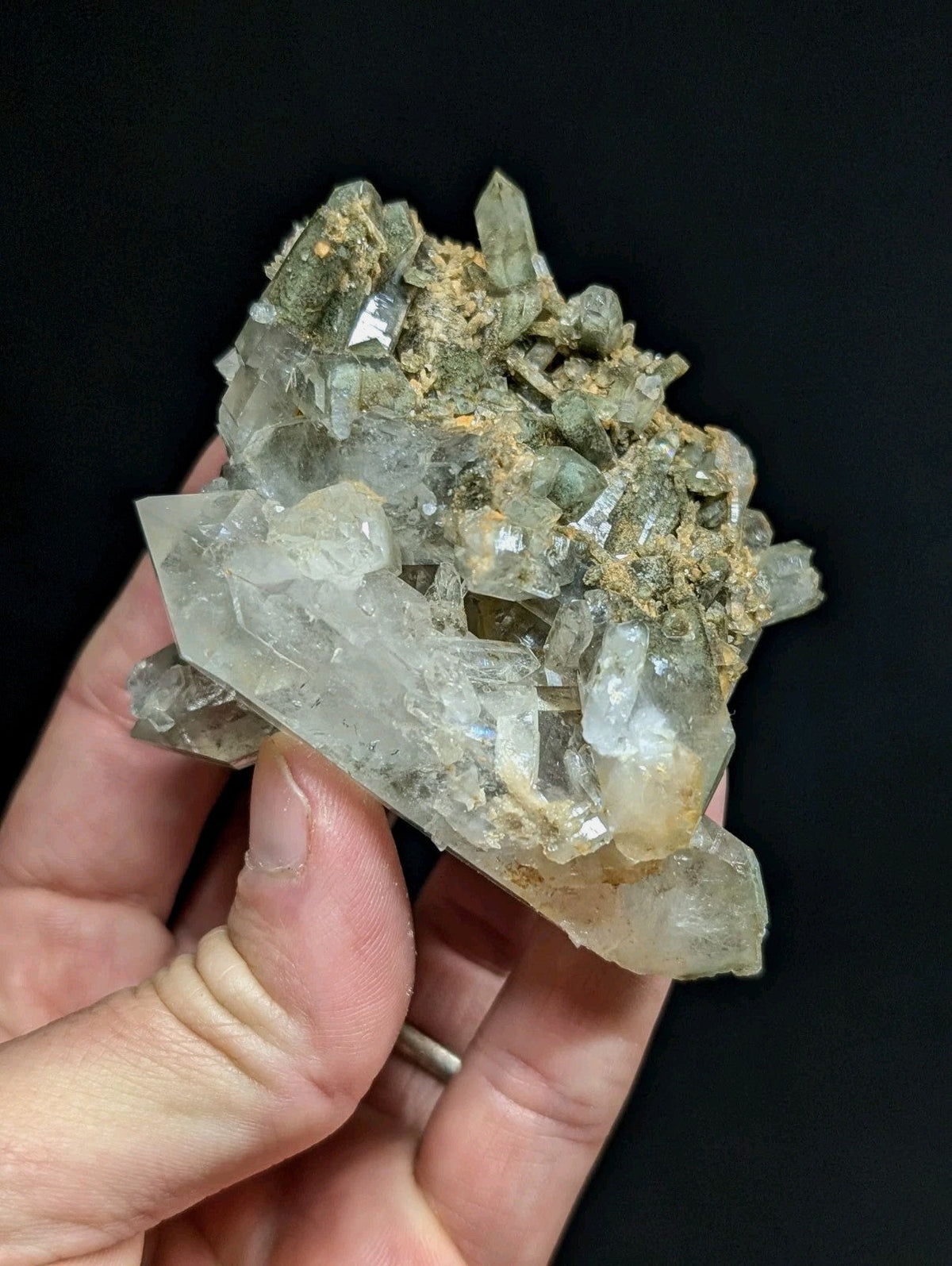 A translucent, clear quartz crystal cluster with some greenish and earthy brown matrix material.