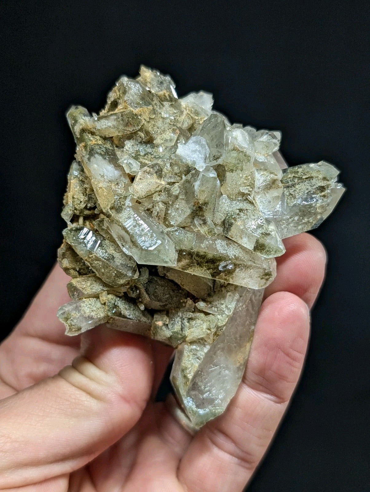 A cluster of translucent, pale green quartz crystals with sharp facets and a natural, earthy matrix.