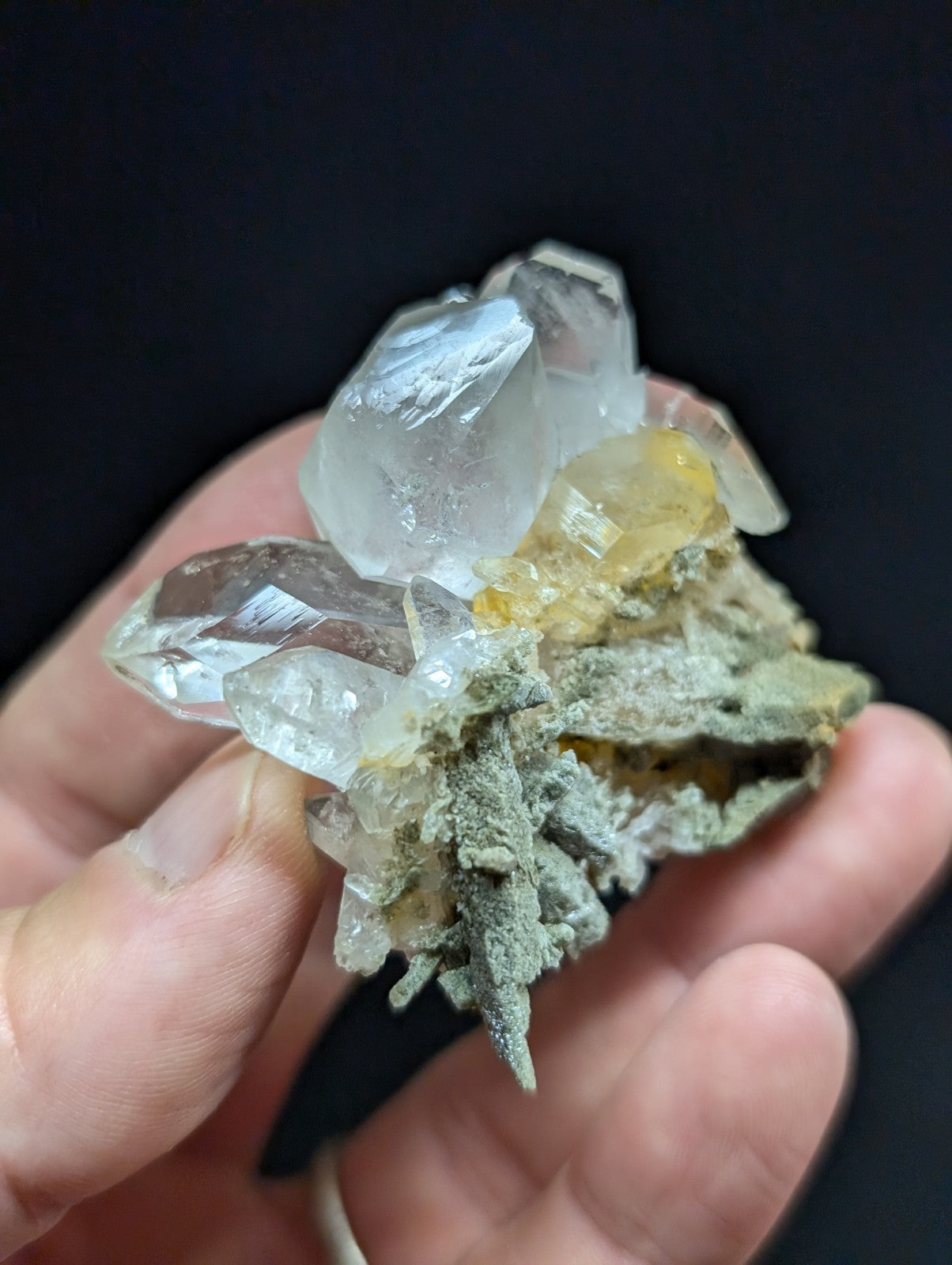 A translucent quartz crystal cluster with clear, faceted points and a yellowish inclusion nestled in gray matrix material.