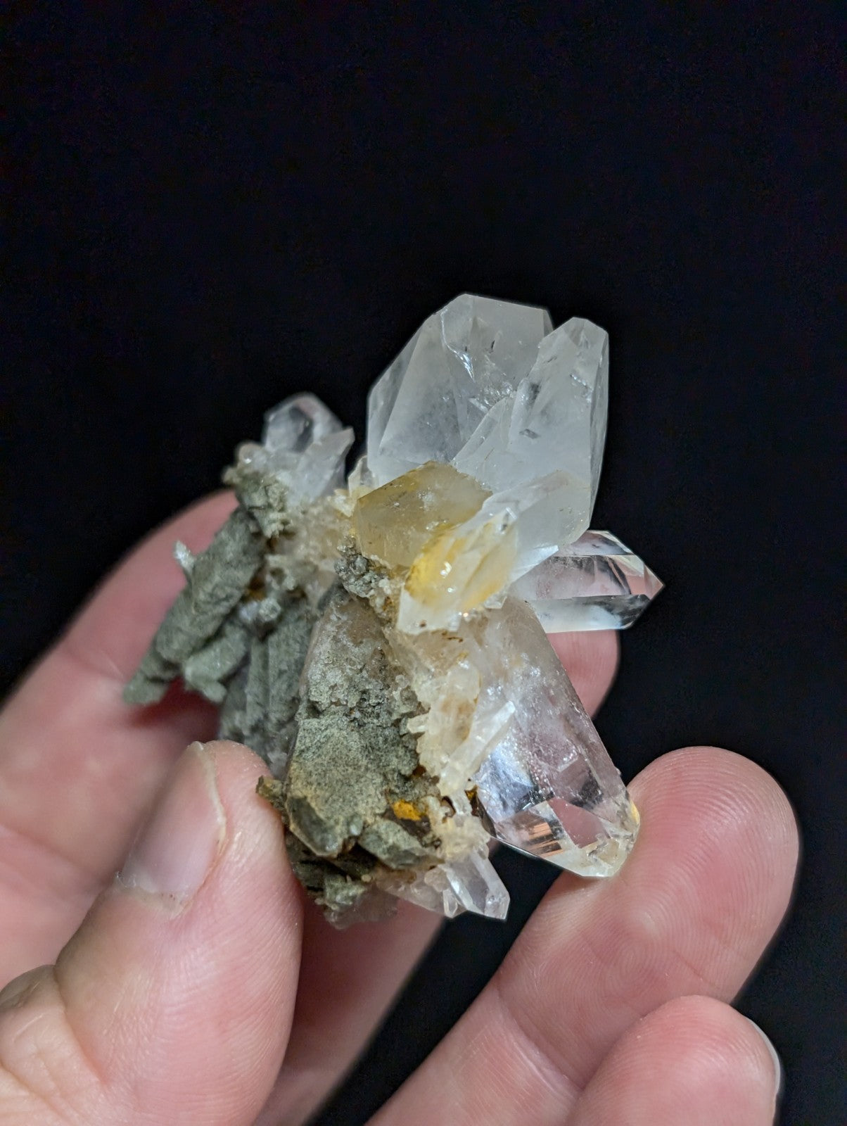 A cluster of clear quartz crystals with a translucent, faceted appearance and some yellowish inclusions, set against a dark background.
