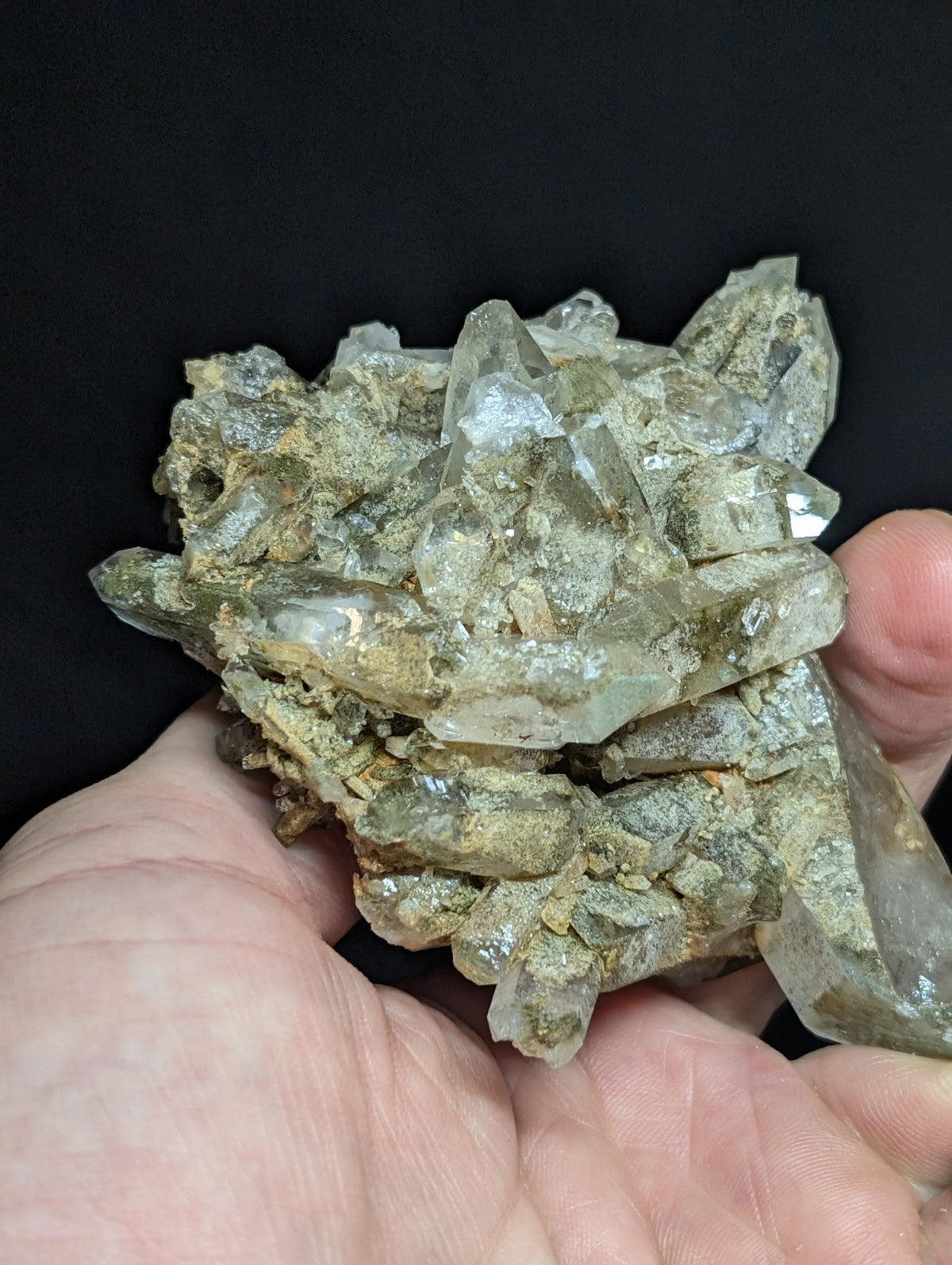 A cluster of translucent, pale greenish quartz crystals with sharp facets and a rough, earthy matrix.