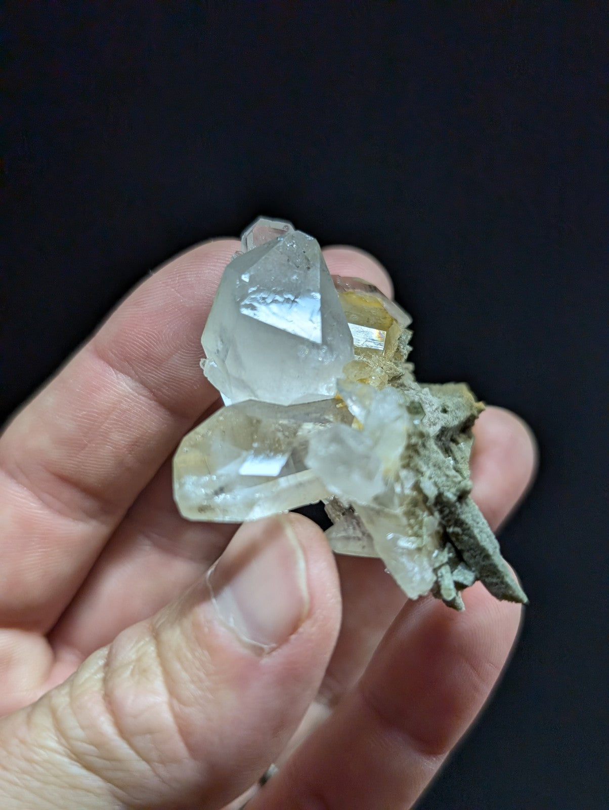 A translucent, clear quartz crystal cluster with sharp facets and a pale yellowish tint nestled in a rough, gray matrix.