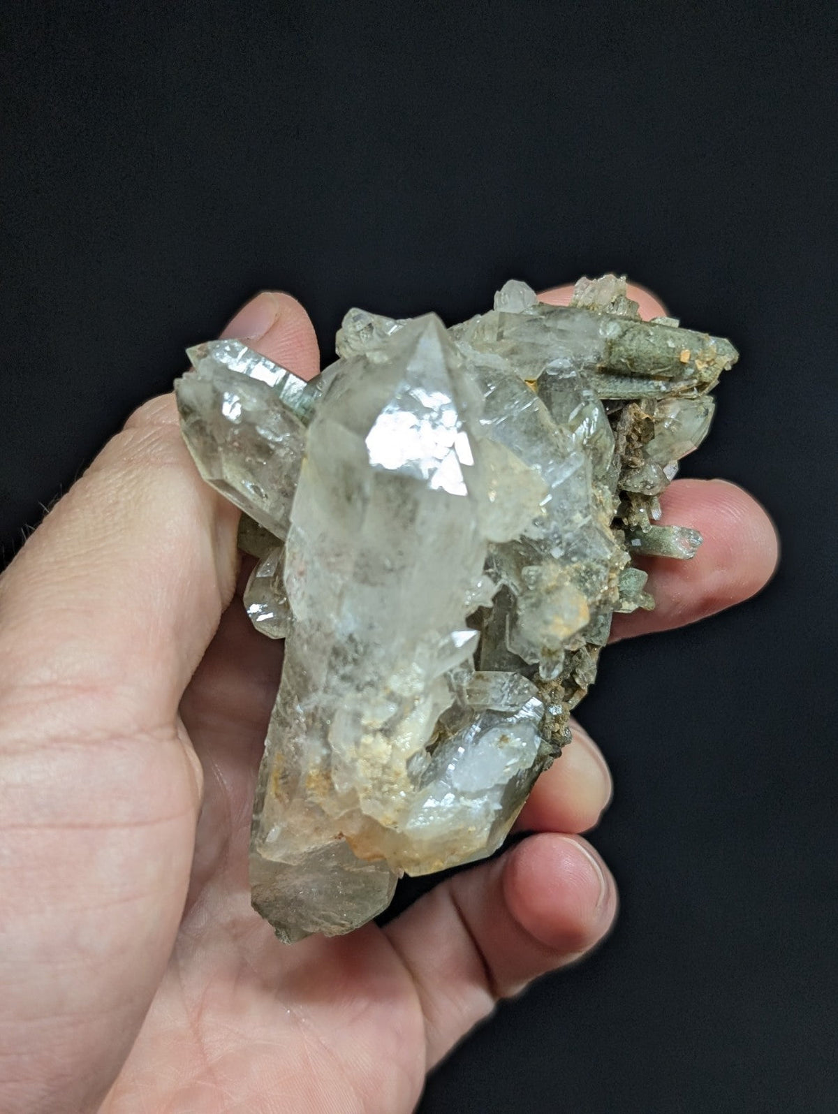 A translucent, clear quartz crystal cluster with a few faint greenish tints and embedded mineral inclusions.