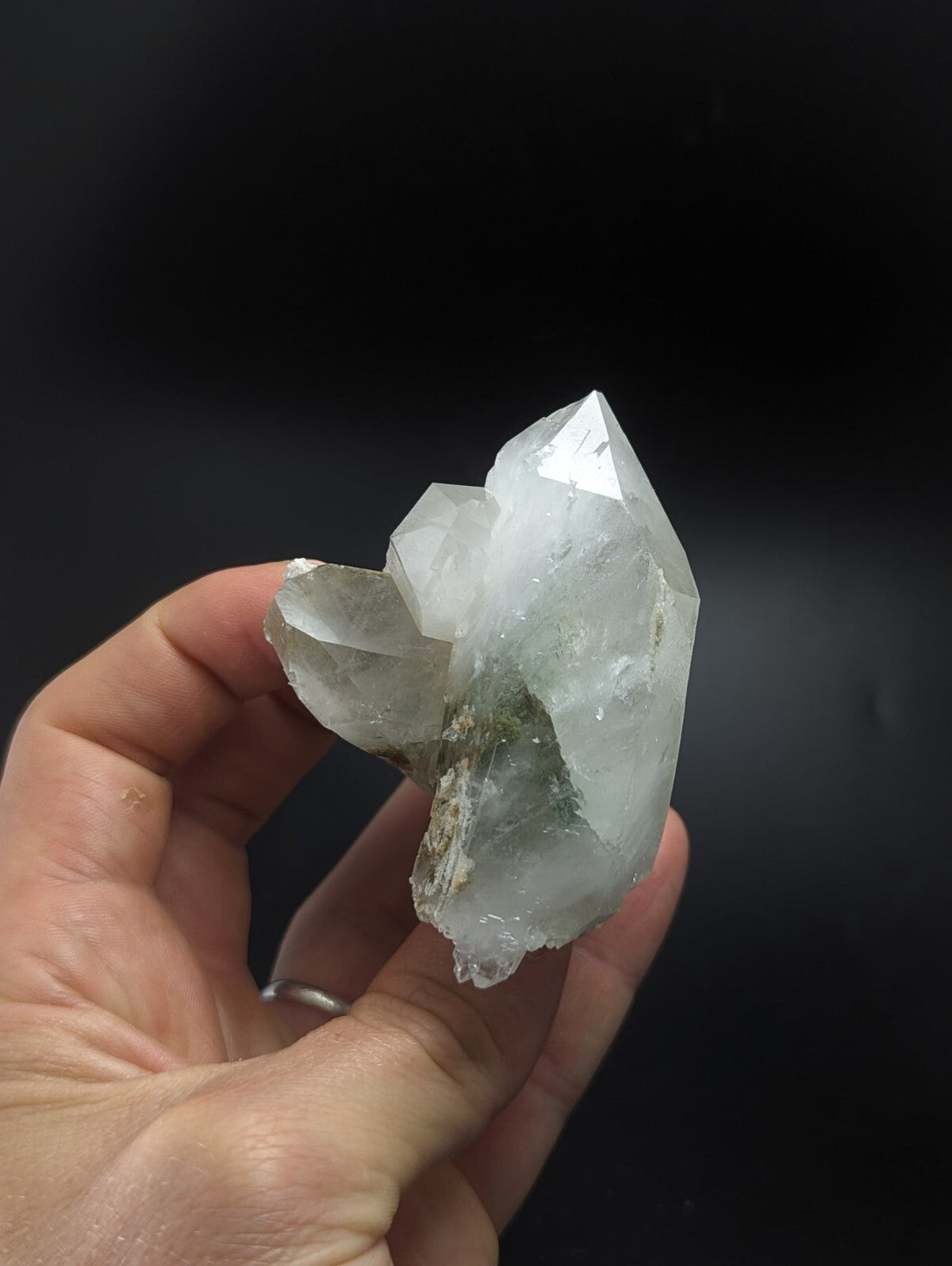 A translucent, clear quartz crystal cluster with sharp geometric facets and a few greenish inclusions.