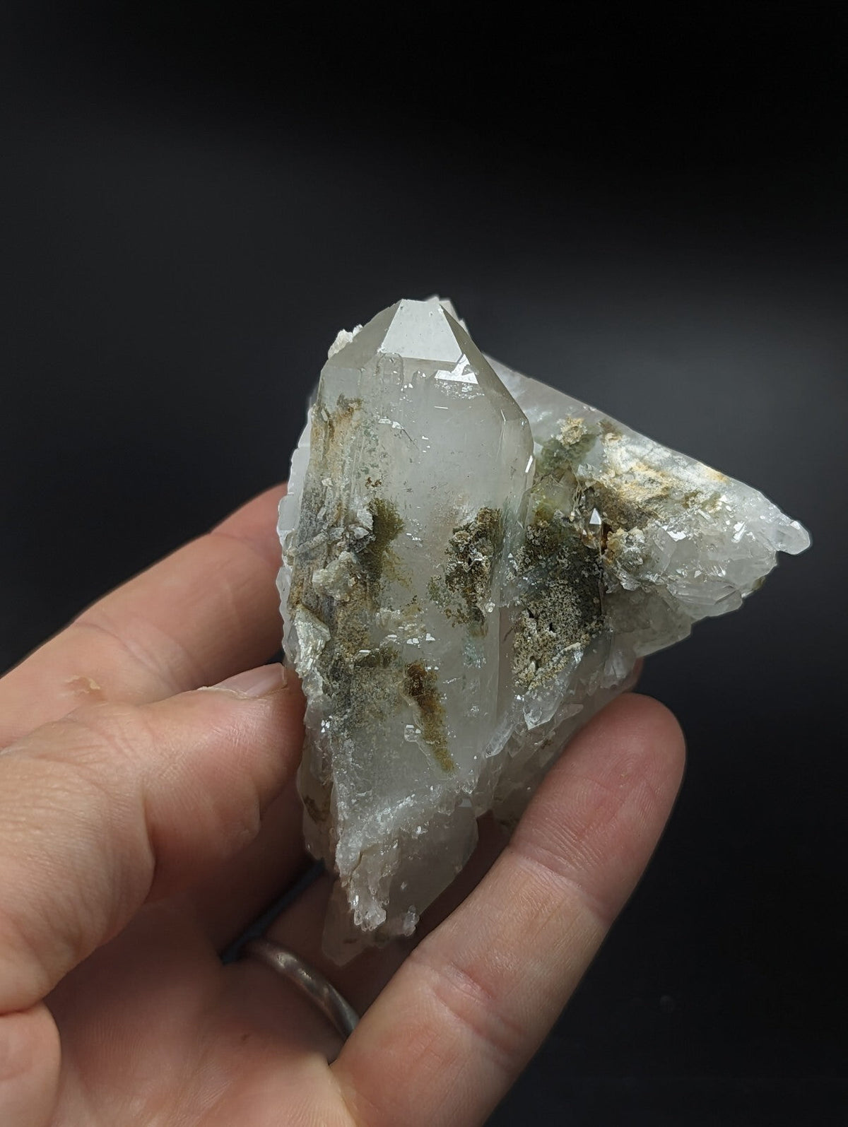 A translucent quartz crystal cluster with greenish mineral inclusions, held gently in a hand.