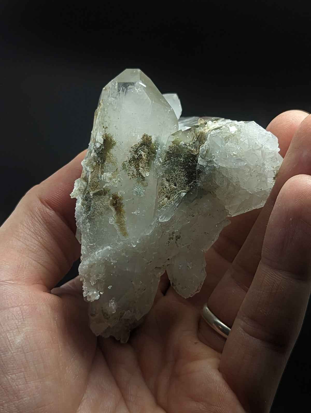 A translucent white quartz crystal cluster with green mossy inclusions, held gently in a hand.