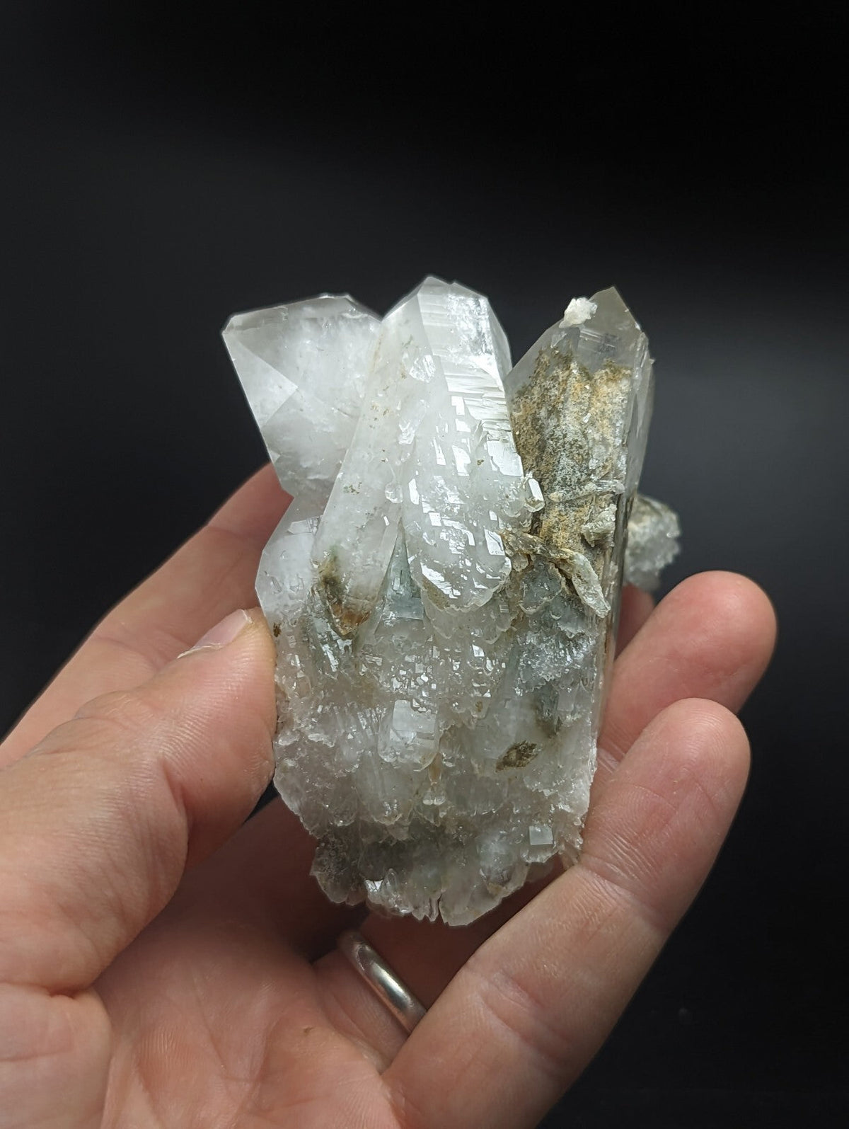 A translucent, clear quartz crystal cluster with some greenish-gray veining and a rough, natural base.