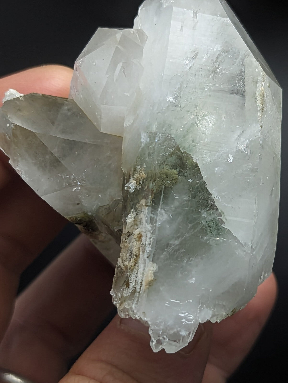 A translucent, clear quartz crystal cluster with some greenish mineral inclusions and a rough, jagged surface.