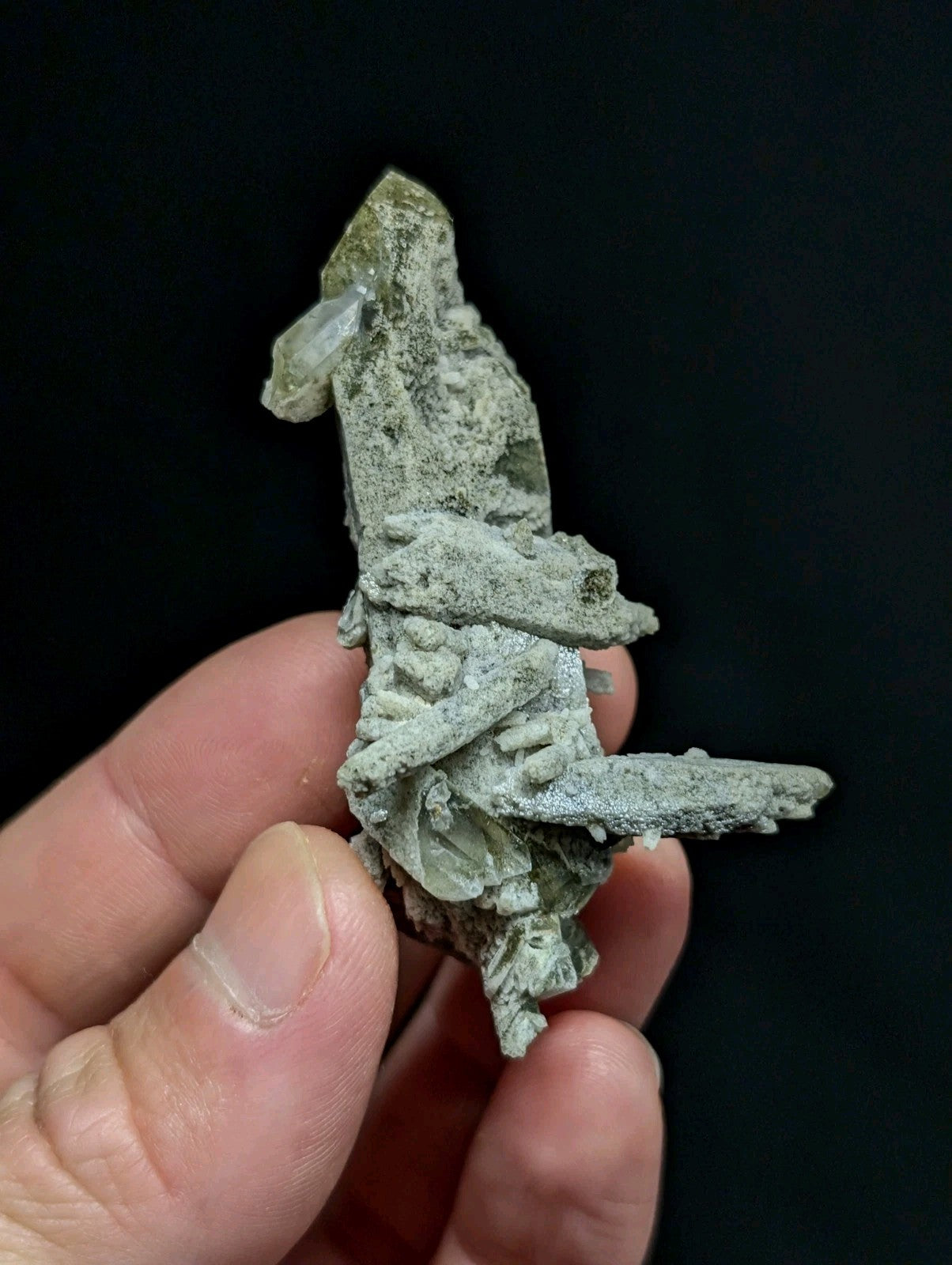 A greenish-gray mineral specimen with a rough, textured surface and translucent crystal formations.