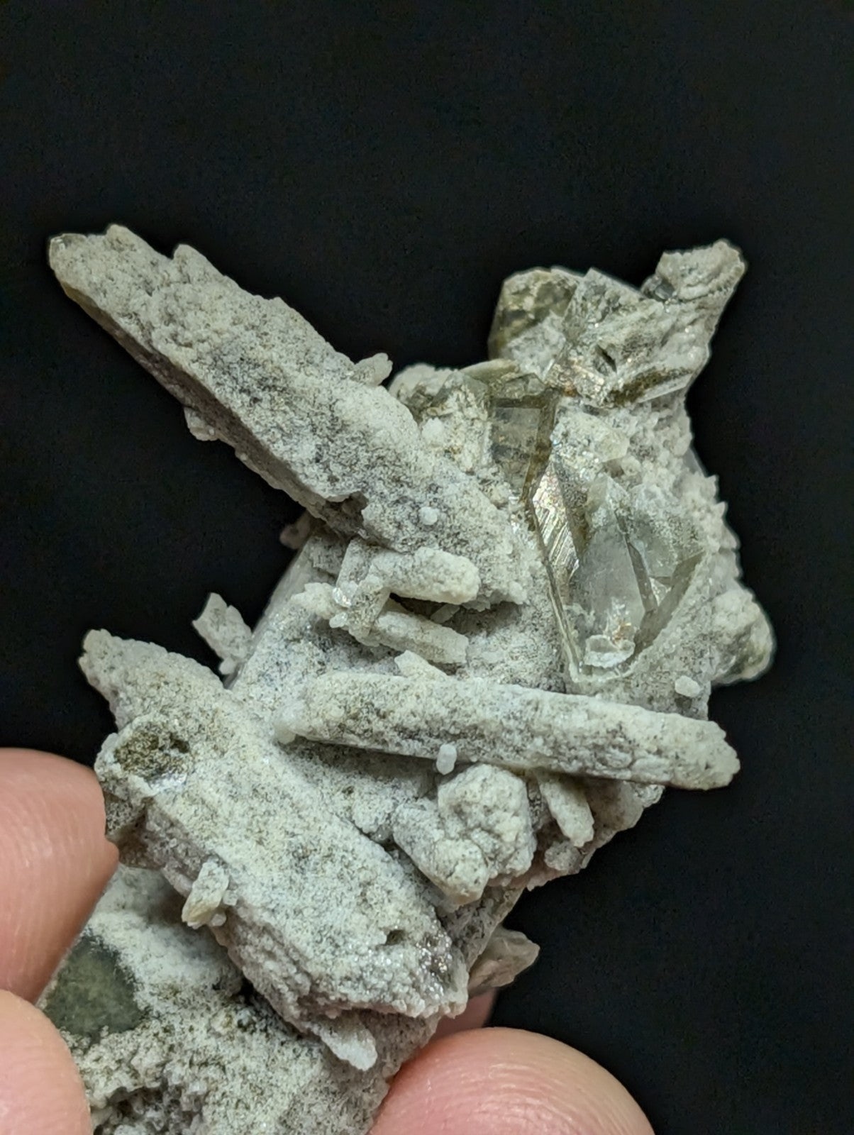 A grayish-green mineral specimen featuring translucent crystal formations embedded in a matrix of earthy, textured material.