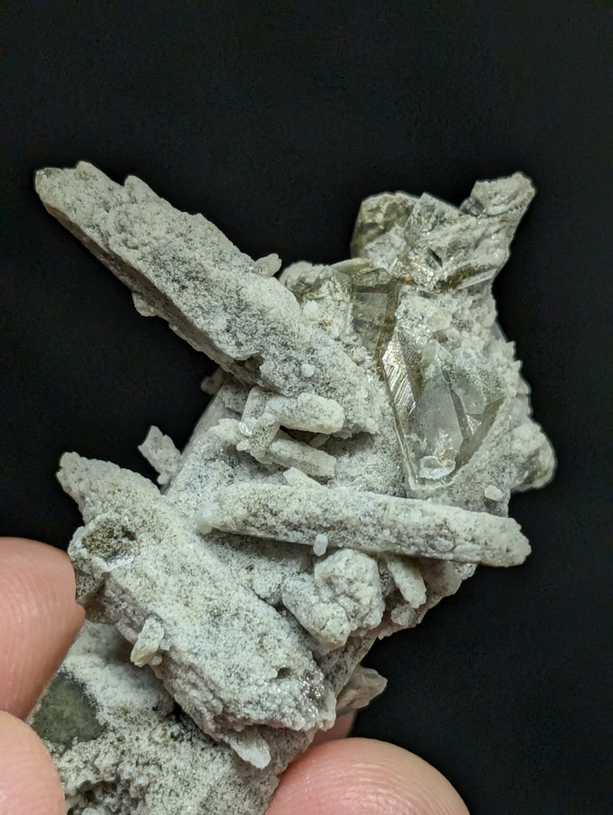 A grayish-green mineral specimen featuring translucent crystal formations embedded in a matrix of earthy, textured material.