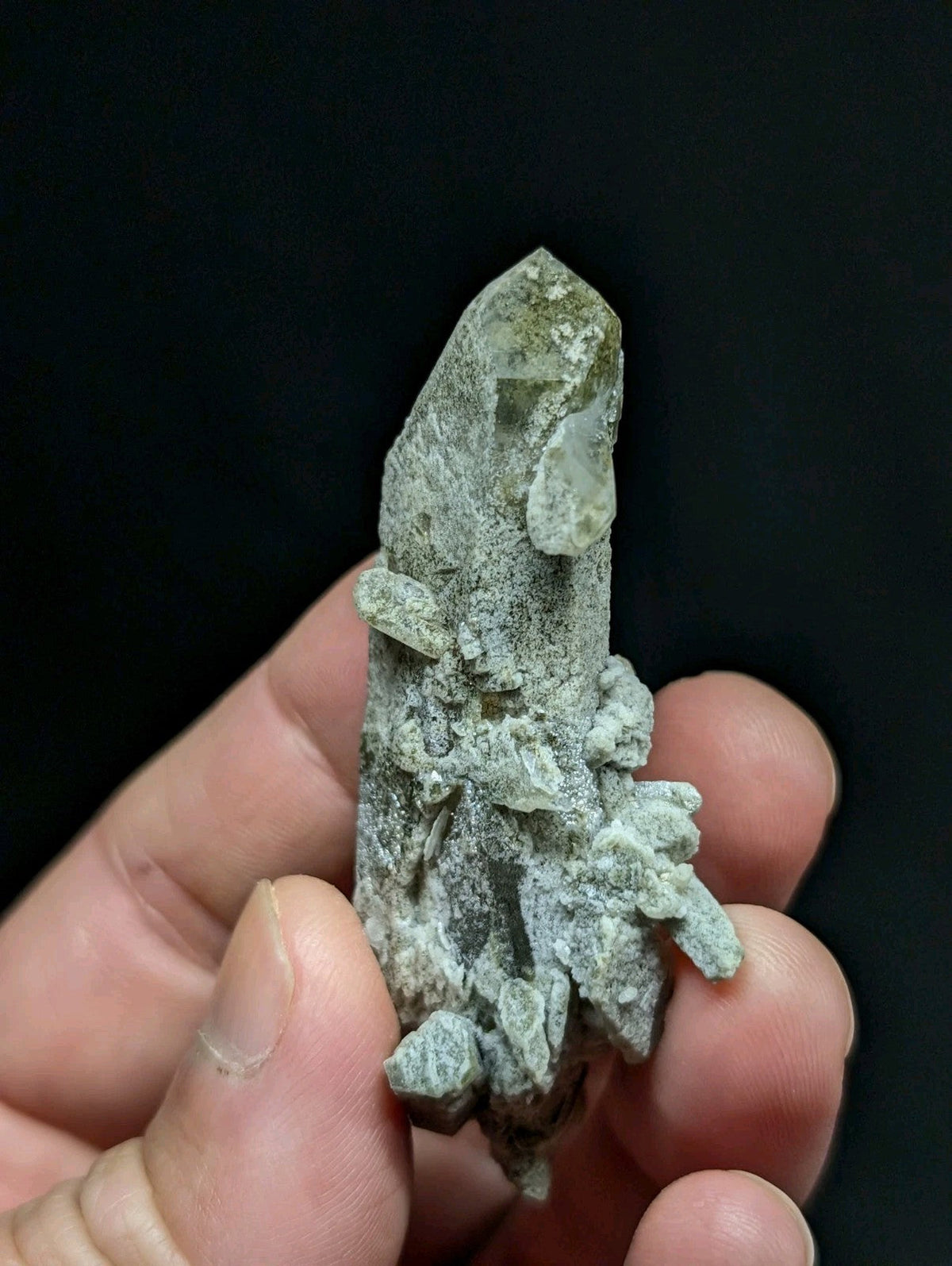 A translucent, pale green quartz crystal with a rough, textured base and pointed tip.