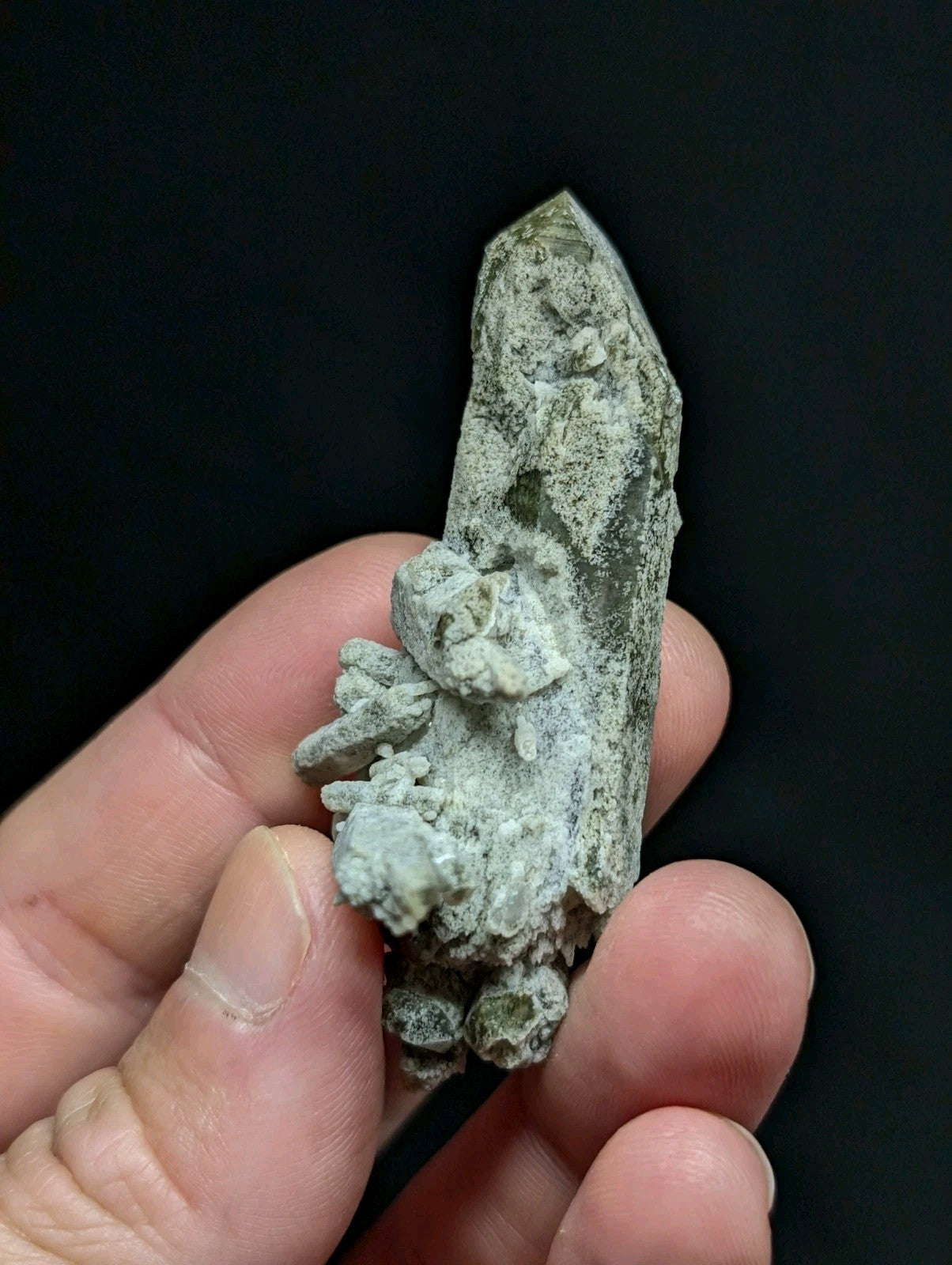A textured, pale green mineral specimen with a pointed crystal tip and rough, clustered base.