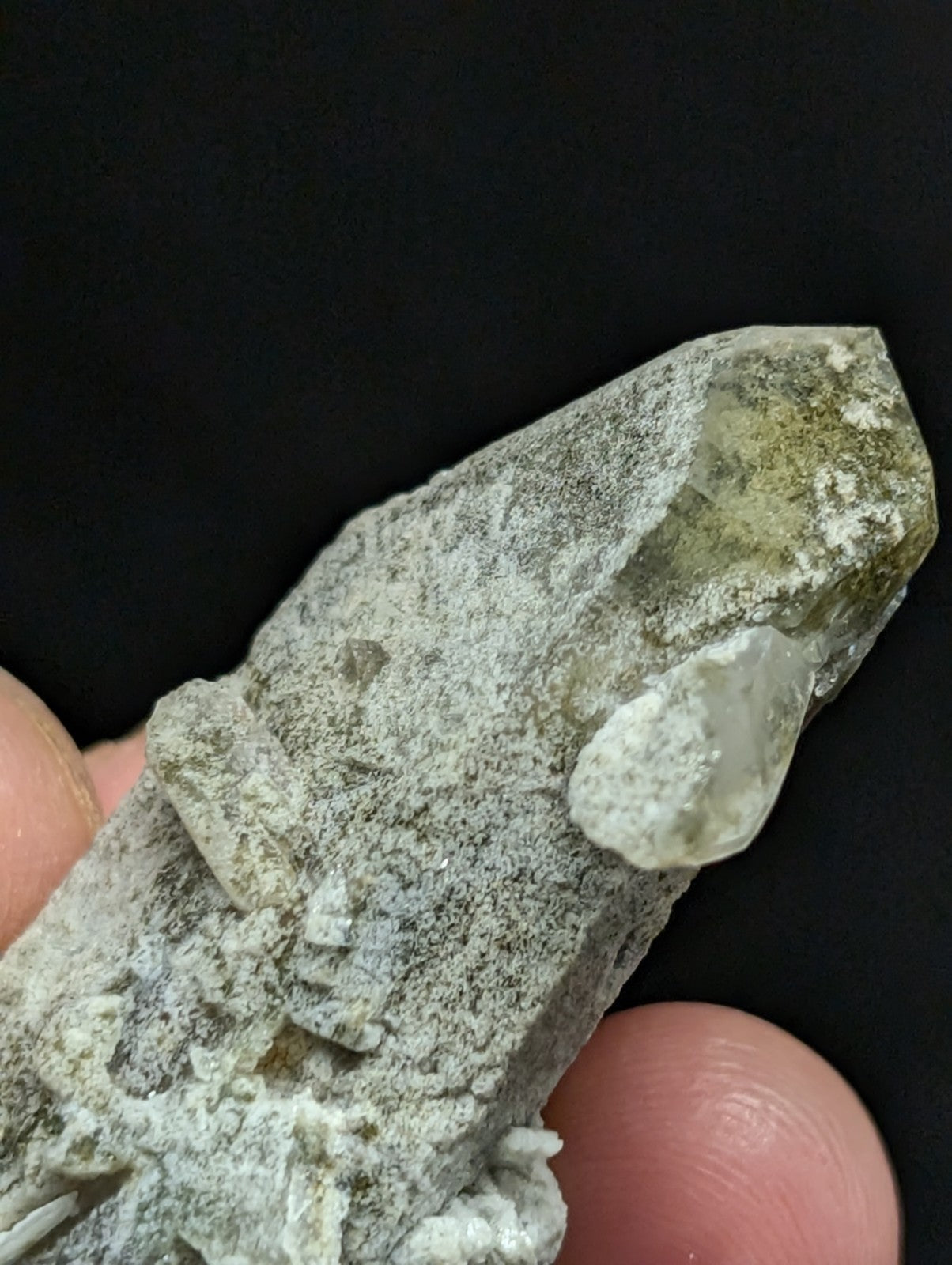 A translucent greenish quartz crystal with a rough, earthy matrix and visible internal inclusions.