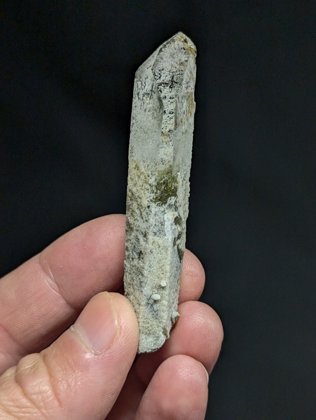 A translucent, pale gray quartz crystal with natural greenish mossy inclusions and a pointed tip.