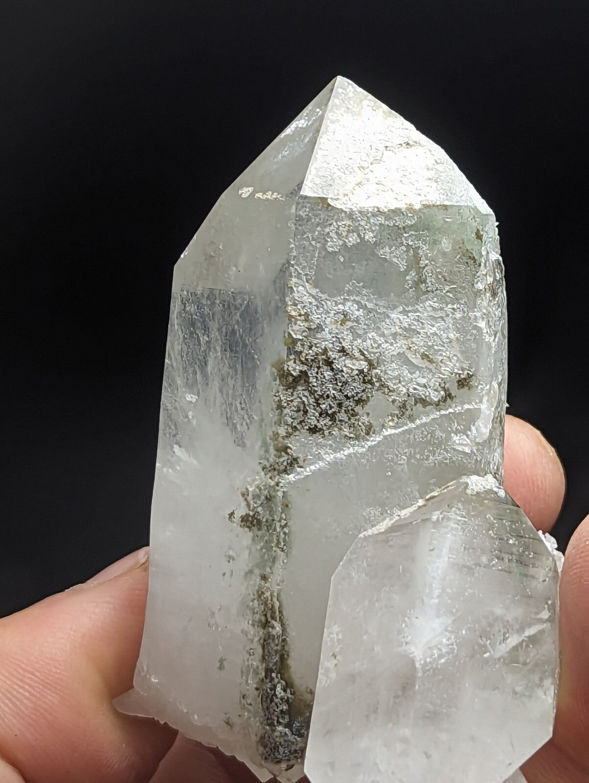 A translucent, clear quartz crystal with a pointed tip and visible internal greenish-gray inclusions.