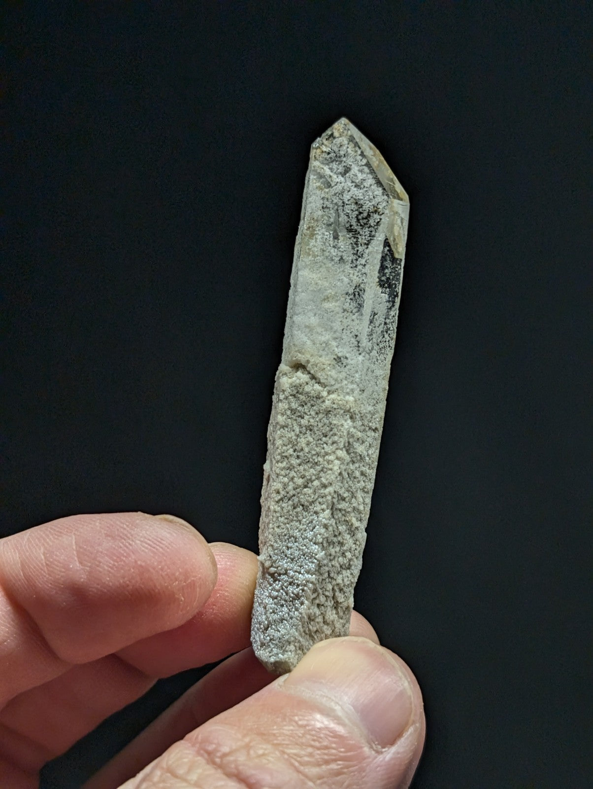 A translucent, pale gray quartz crystal with a pointed tip and rough, textured base.