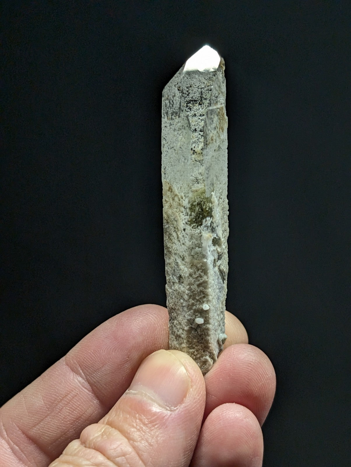 A hand holds a translucent, pale gray quartz crystal with a pointed tip and visible mineral inclusions.