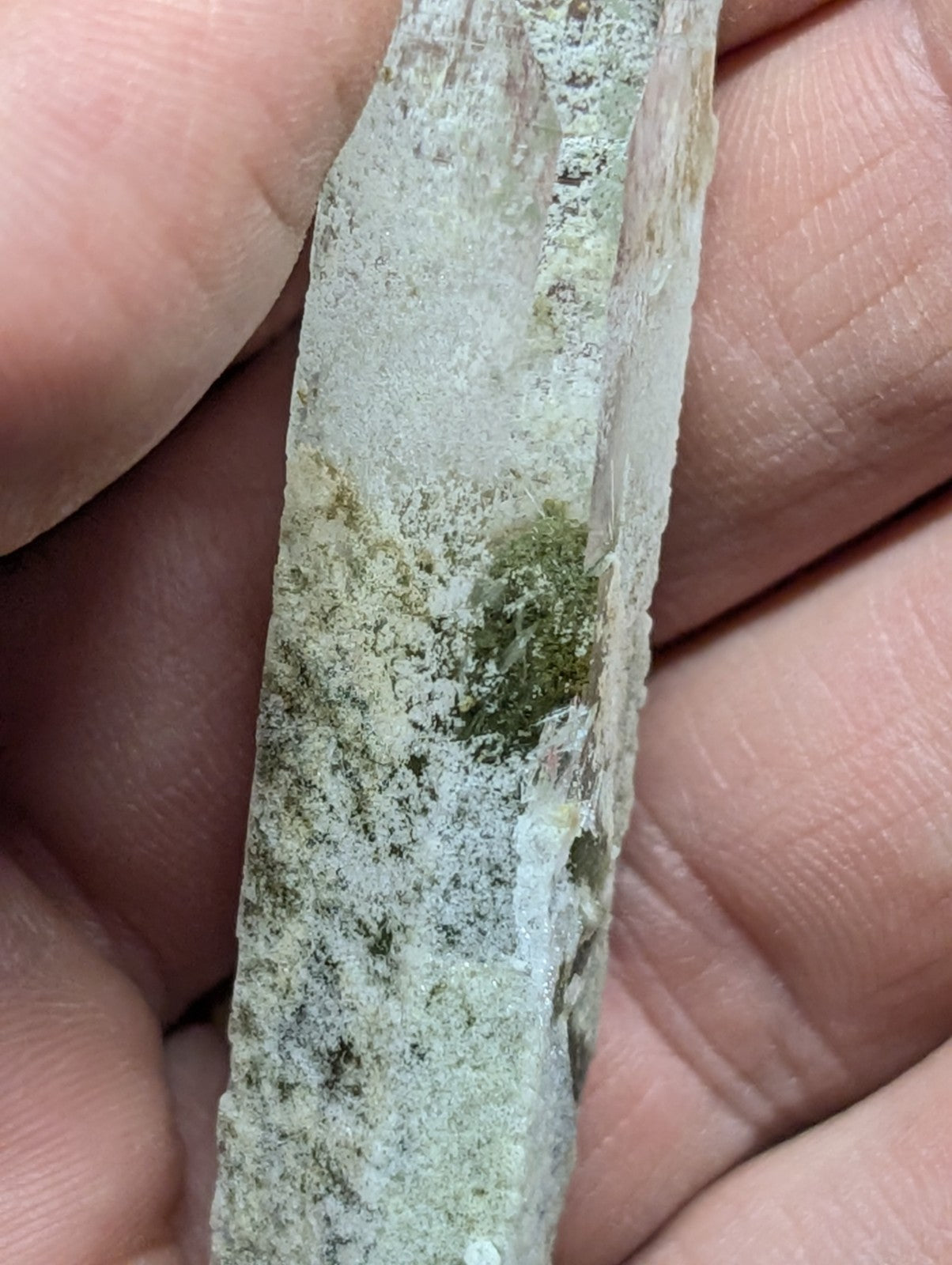 A translucent, pale greenish-white mineral specimen with patches of mossy green growth and a rough, naturally fractured surface.