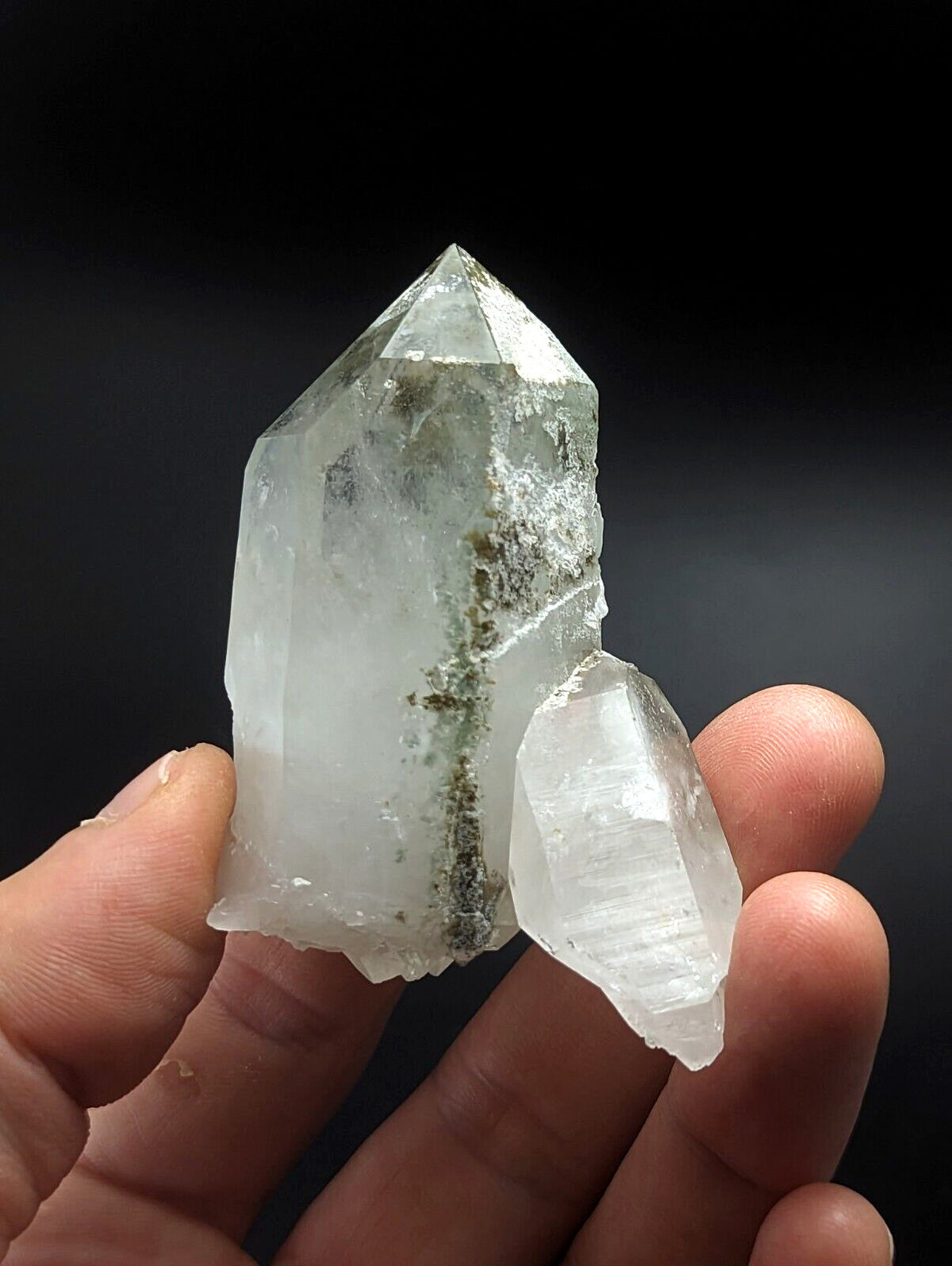 A translucent, clear quartz crystal cluster with a prominent vertical vein of greenish mineral inclusions.