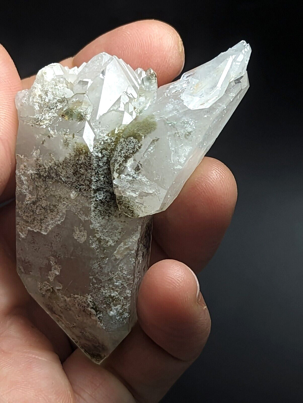 A translucent, clear quartz crystal cluster with sharp geometric facets and patches of green moss growth.