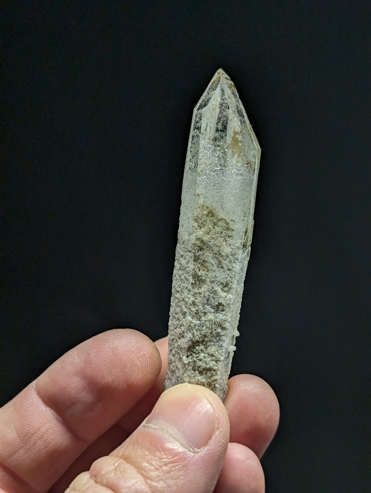 A translucent, pointed quartz crystal with a rough, speckled surface and subtle greenish inclusions.