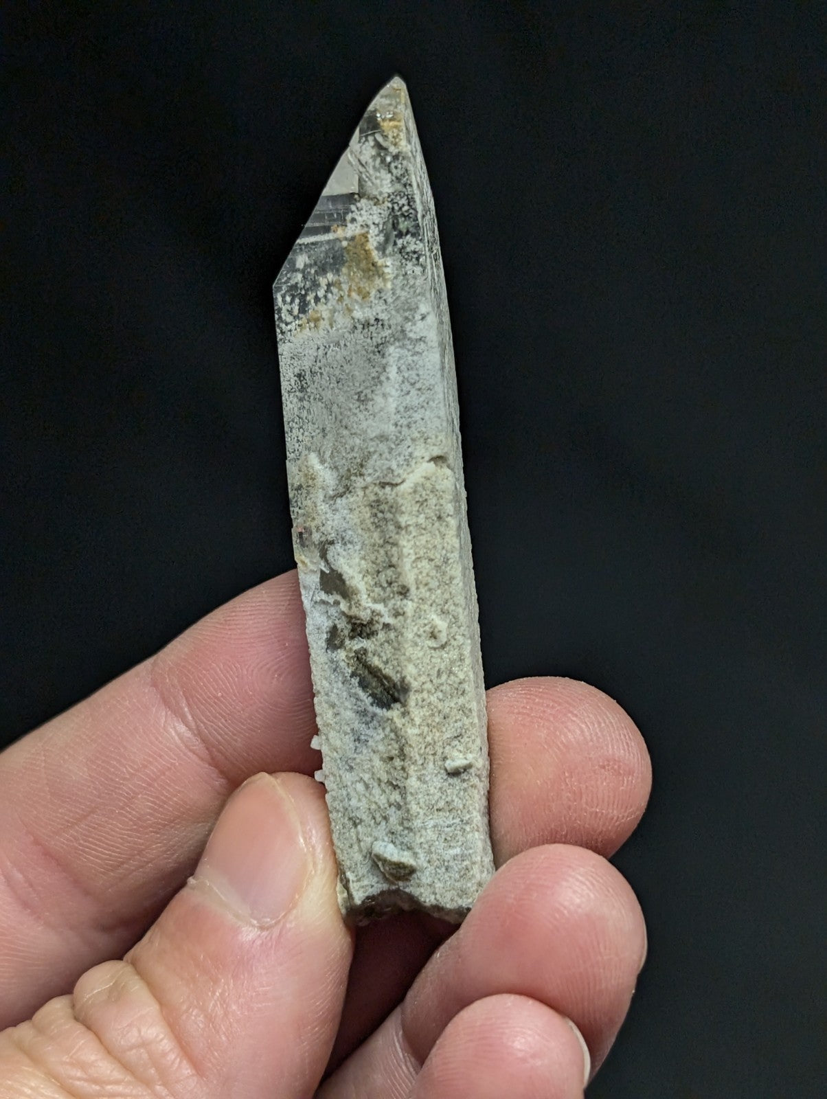 A weathered, translucent quartz crystal with a pointed tip and speckled grayish-green surface.