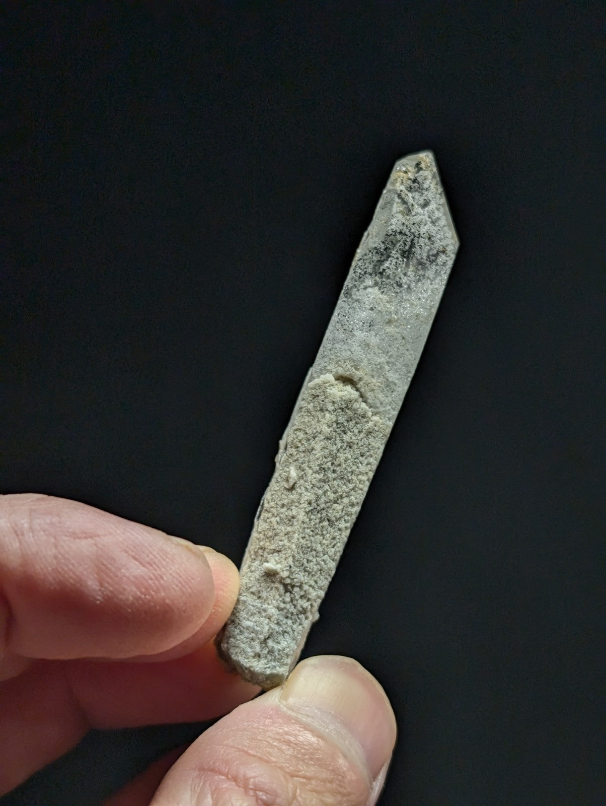 A weathered, grayish-green quartz crystal point with a rough, textured surface and pointed tip.