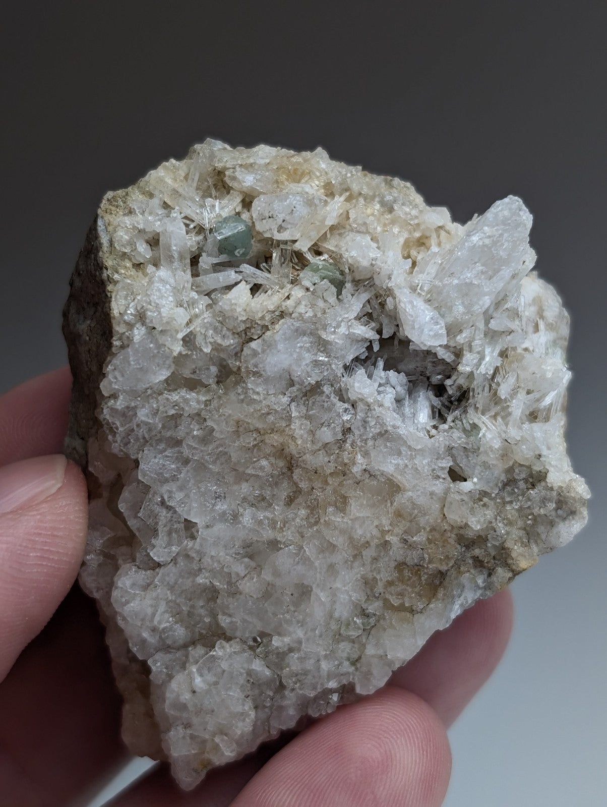 A hand holds a rare green cookeite mineral with translucent white and pale green crystals on dark solution quartz from Arkansas