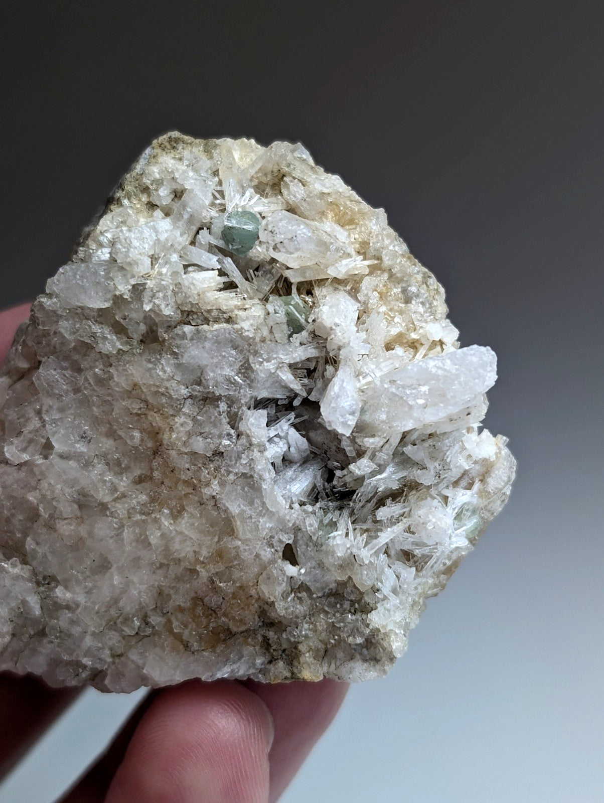 A hand holds green cookeite on translucent white solution quartz with green accents rare uv reactive mineral