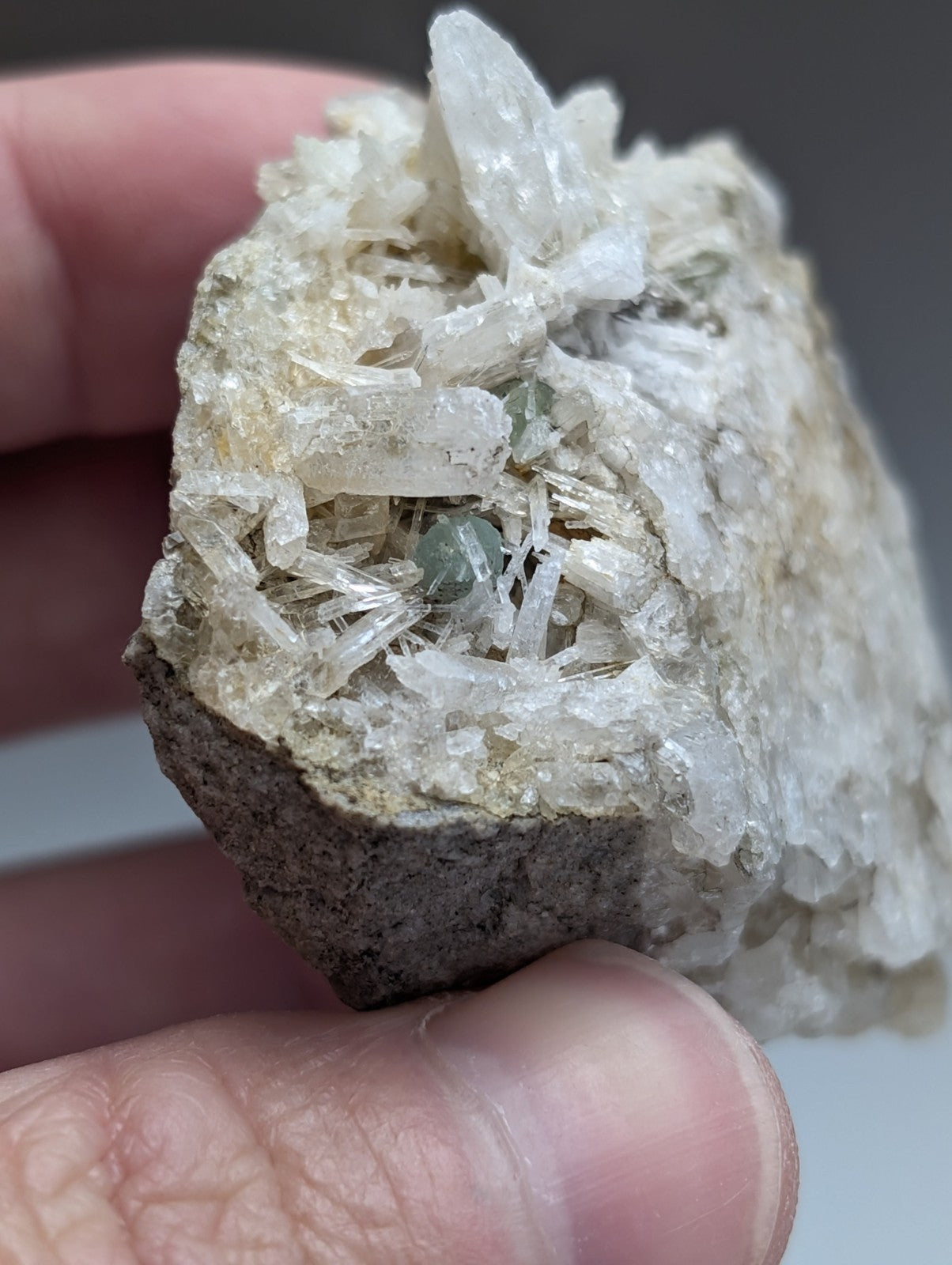 A hand holds a rough dark gray green cookeite on translucent white quartz with greenish minerals from Saline County Arkansas