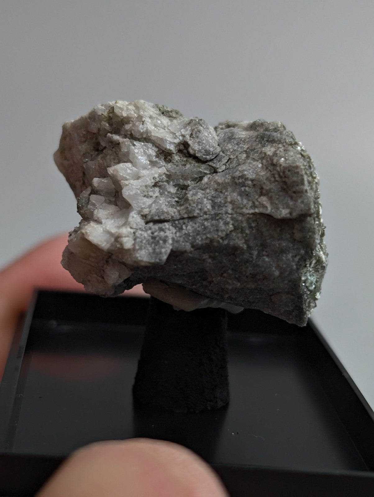 A rough, grayish-white mineral specimen with crystalline formations and a textured surface.