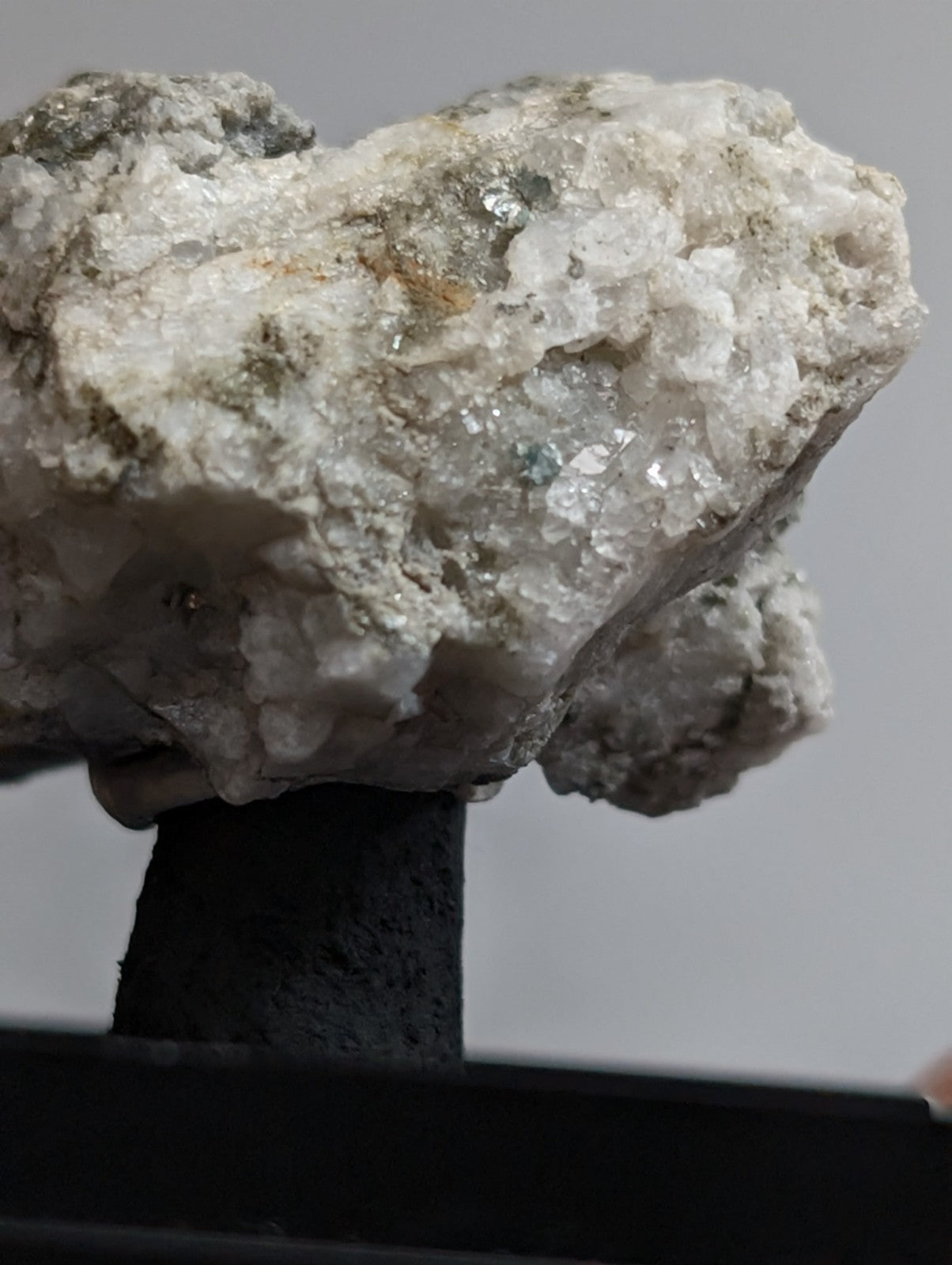A rough, white crystalline mineral specimen with patches of green and gray matrix.