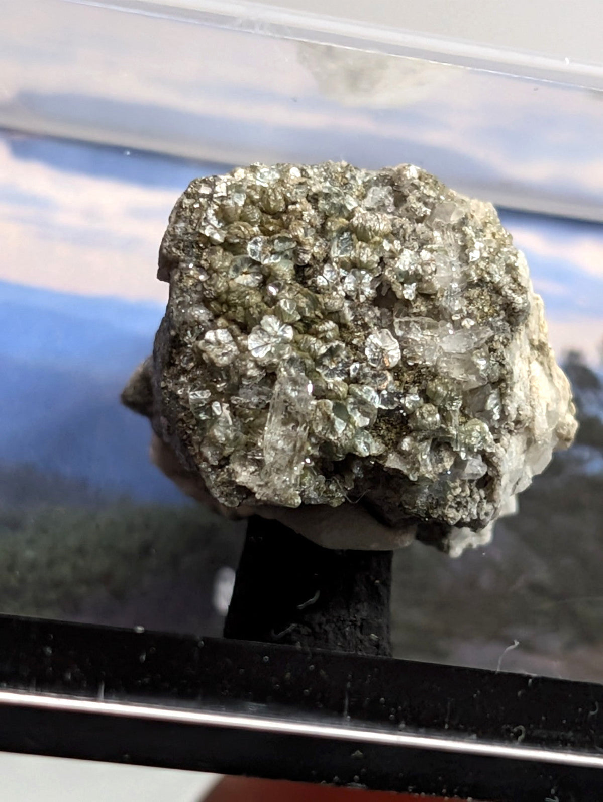 A textured, irregularly shaped mineral specimen with a mix of metallic silver and translucent greenish crystals embedded in a darker matrix.