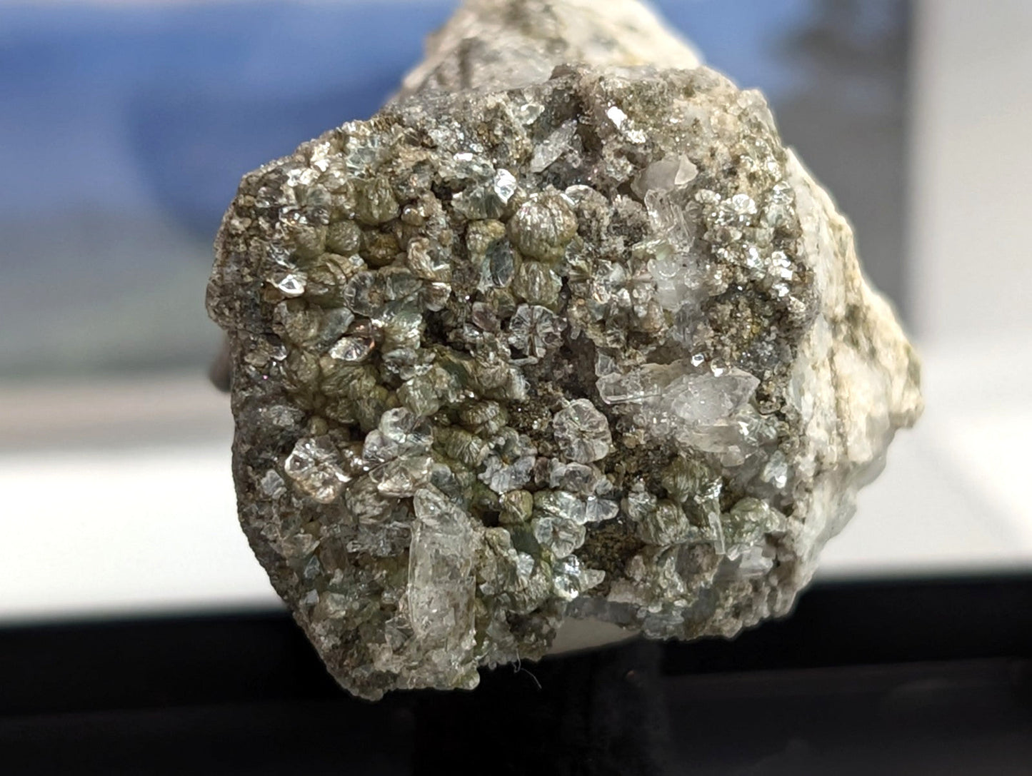 A rough, irregularly shaped mineral specimen featuring a dense cluster of translucent greenish-gray crystals embedded in a lighter gray matrix.