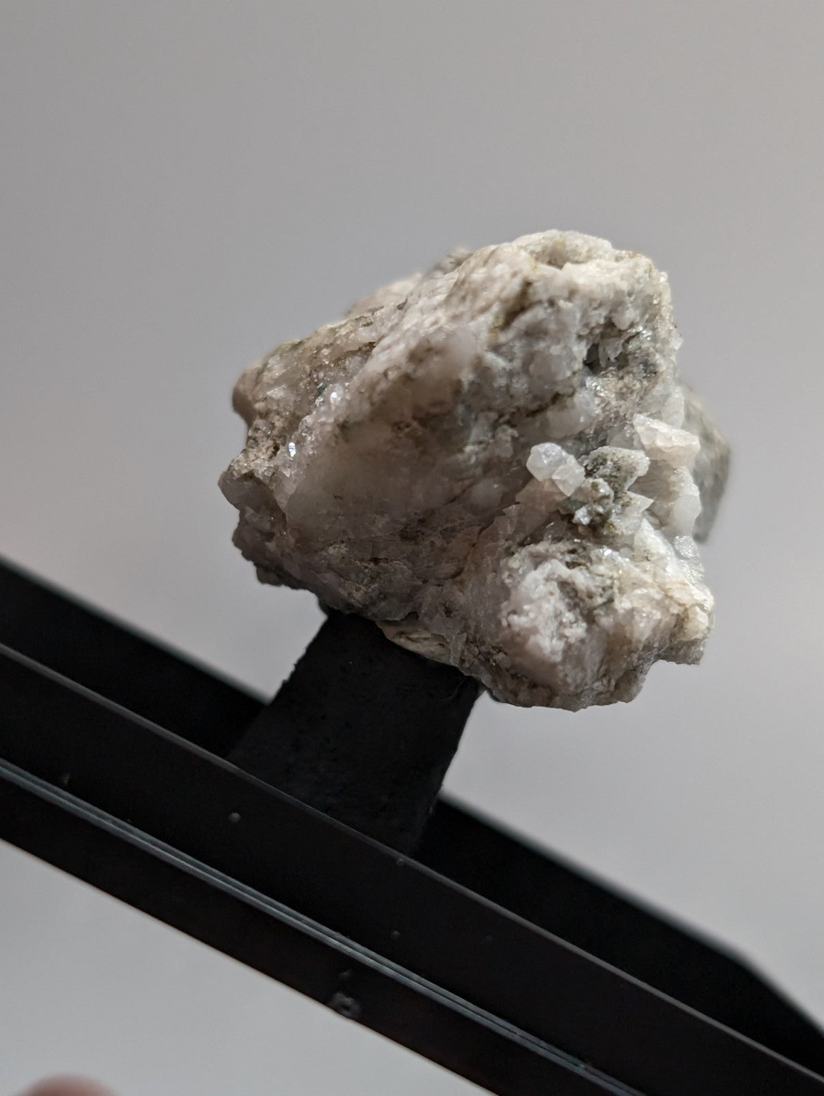 A rough, light gray mineral specimen with crystalline formations and a slightly textured surface.