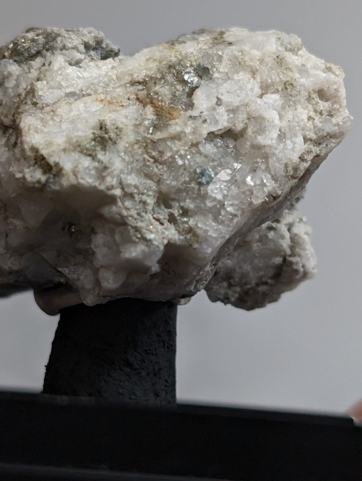 A rough, white crystalline mineral specimen with patches of green and gray matrix.