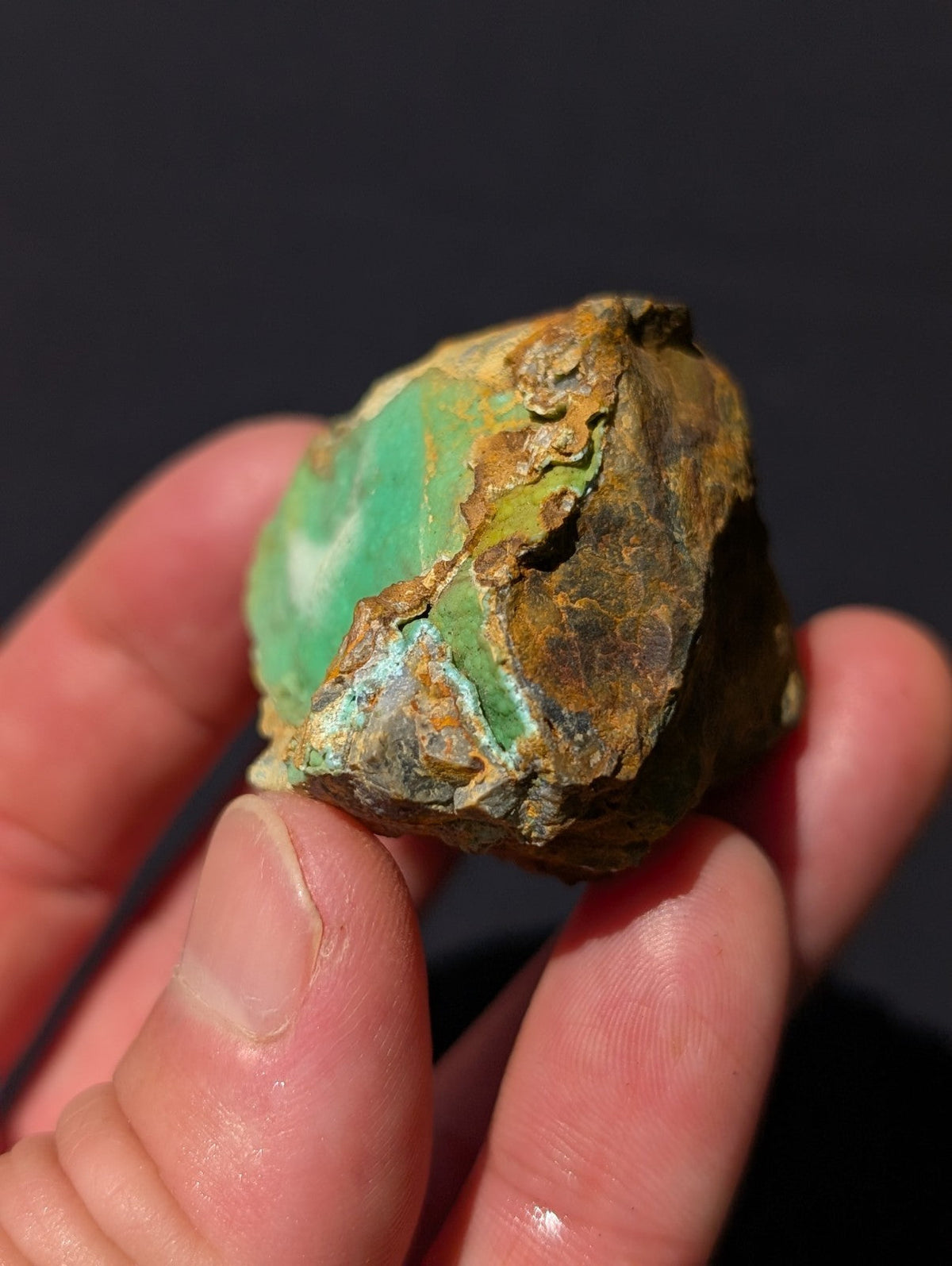 A rough, irregularly shaped turquoise stone with vibrant green patches and earthy brown matrix.