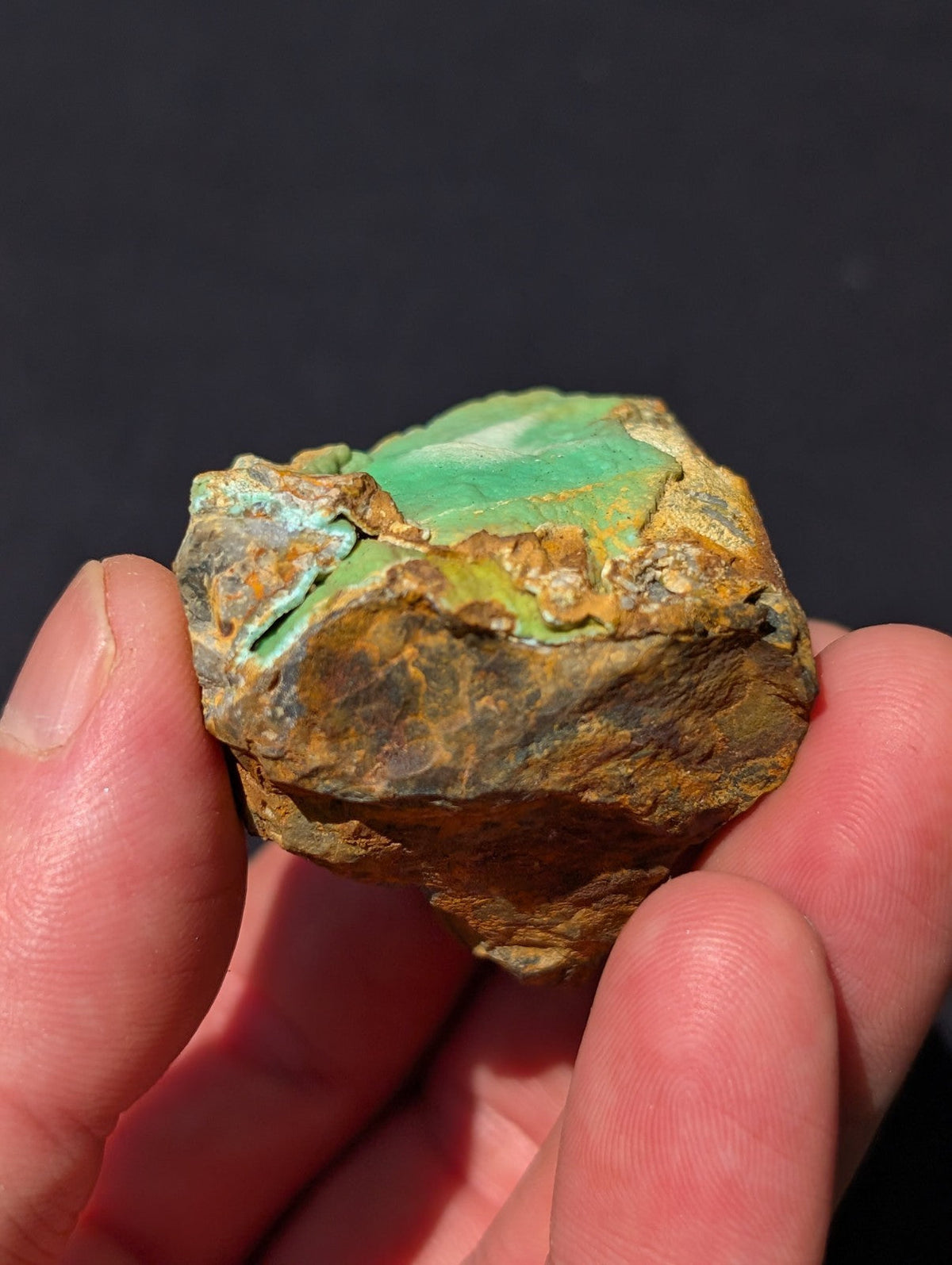 A rough, naturally occurring turquoise stone with a vibrant greenish-blue surface and earthy brown matrix.