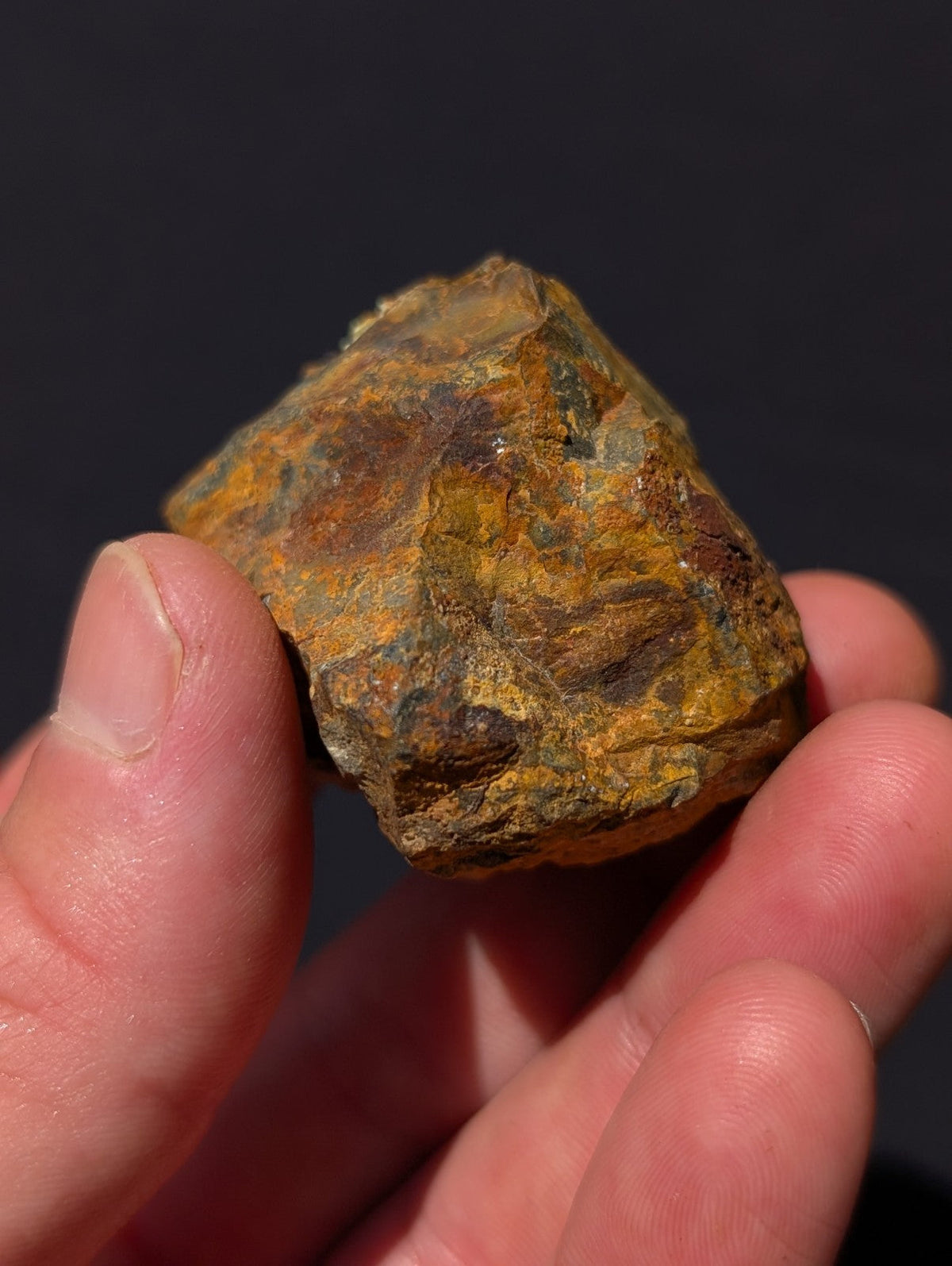 A rough, irregularly shaped mineral specimen with a textured surface displaying patches of yellowish-orange and dark brown hues.