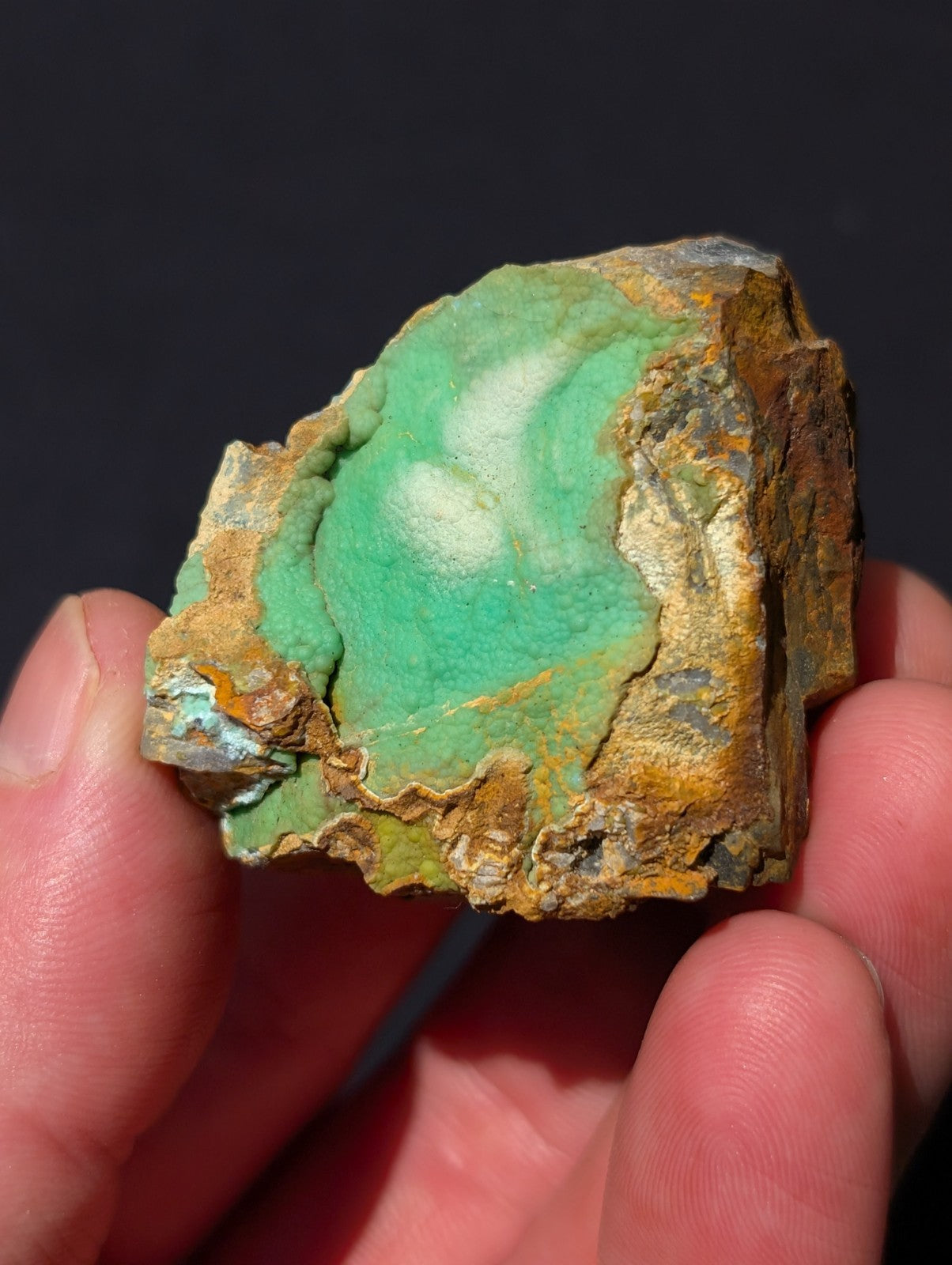 A hand holds a rough, irregularly shaped piece of turquoise mineral with vibrant greenish-blue coloration and earthy brown matrix.