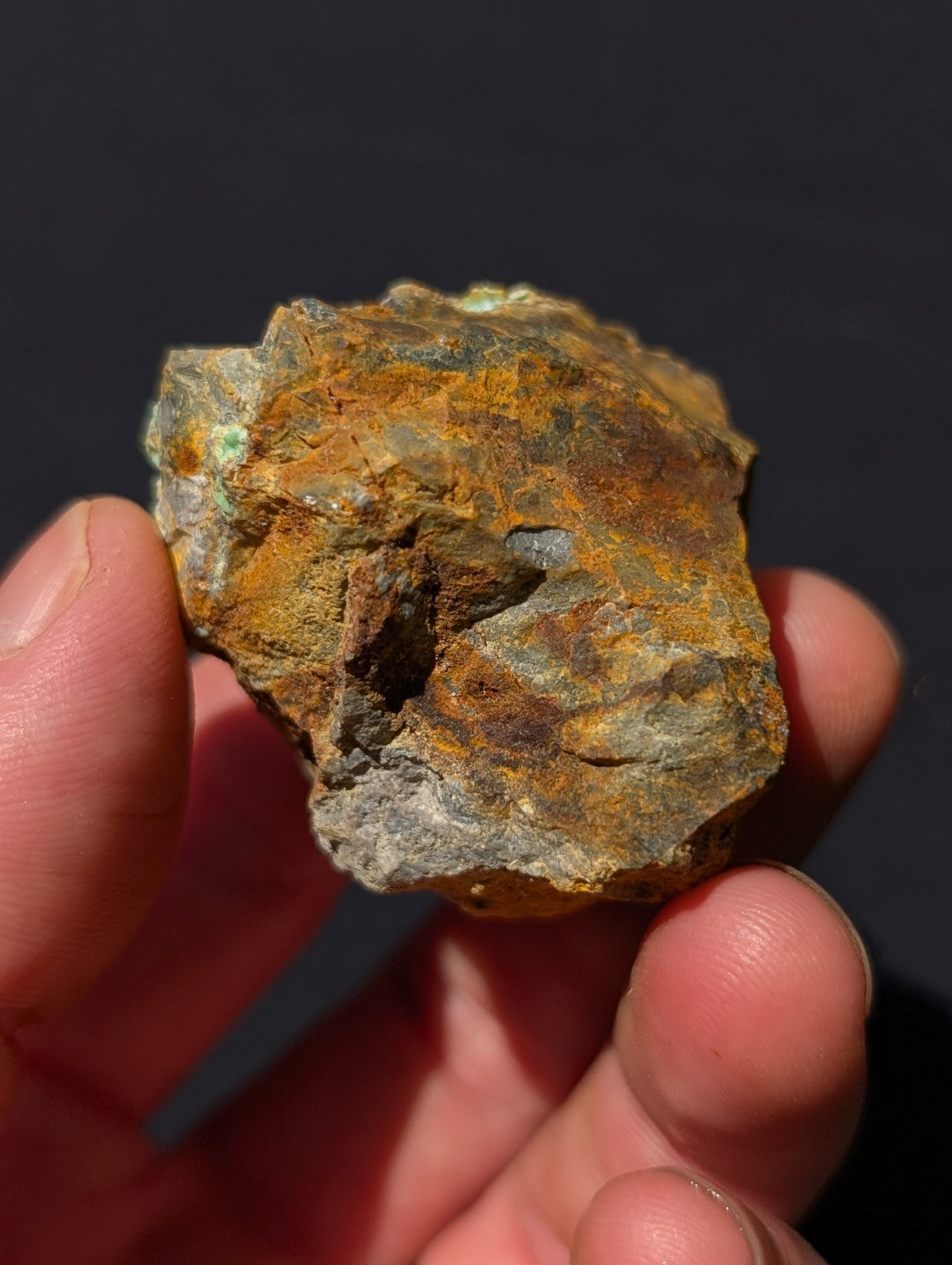 A rugged, irregularly shaped rock with a textured surface displaying patches of orangey-brown rust and greenish patina.