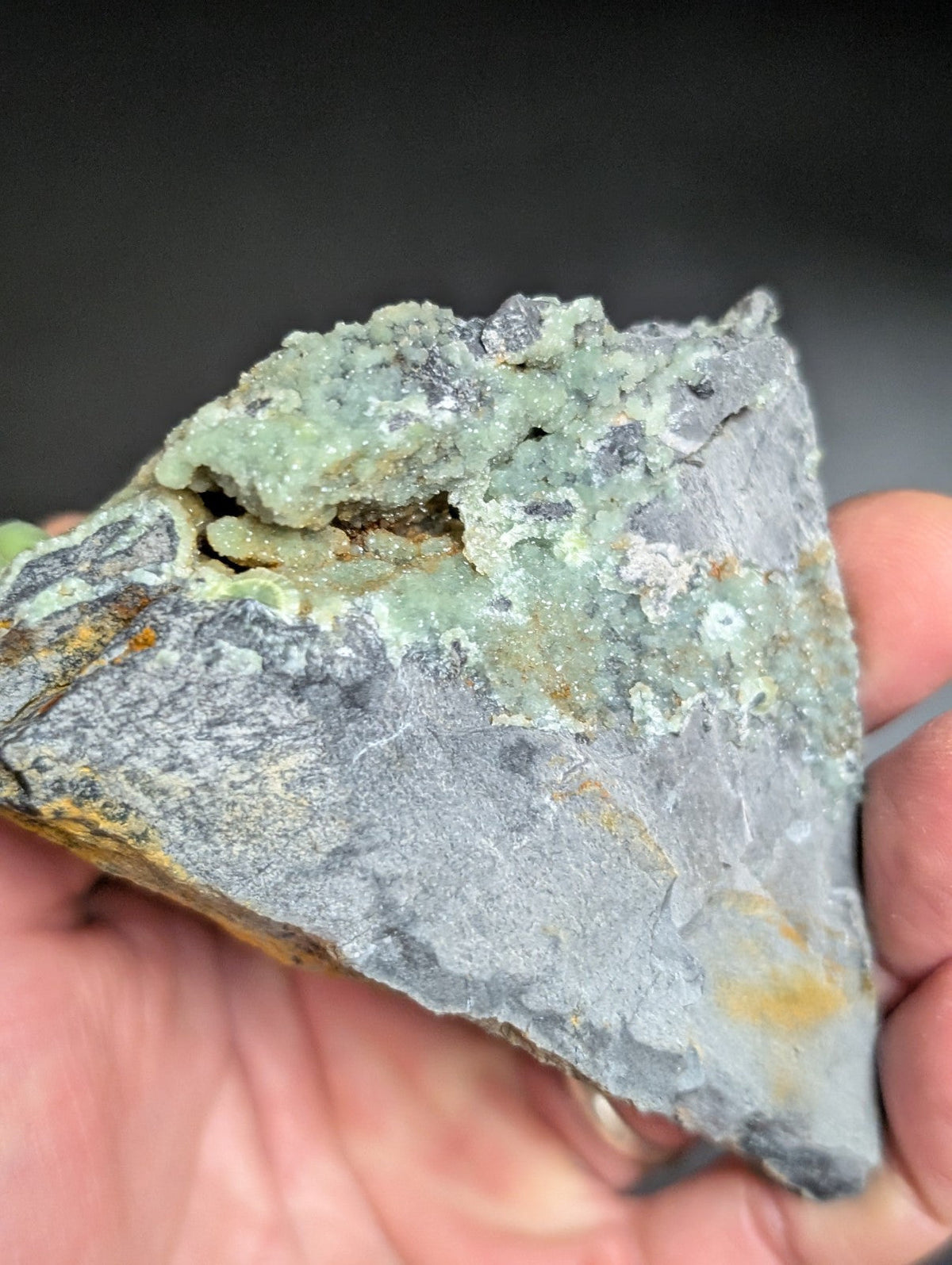 A rough, irregularly shaped mineral specimen with a gray base and patches of greenish-blue crystalline growths.