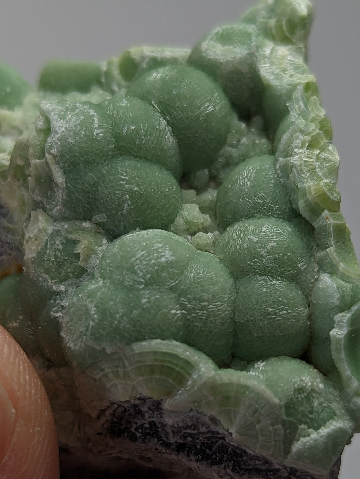 A cluster of translucent, pale green spherical crystals with a rough, textured surface and subtle white veining.