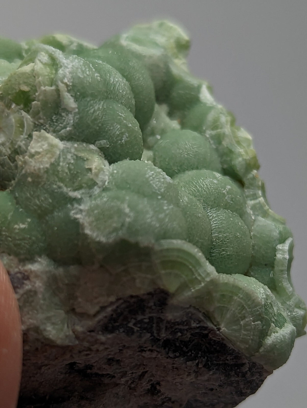 A cluster of translucent, pale green spherical crystals with a waxy sheen and subtle striations.