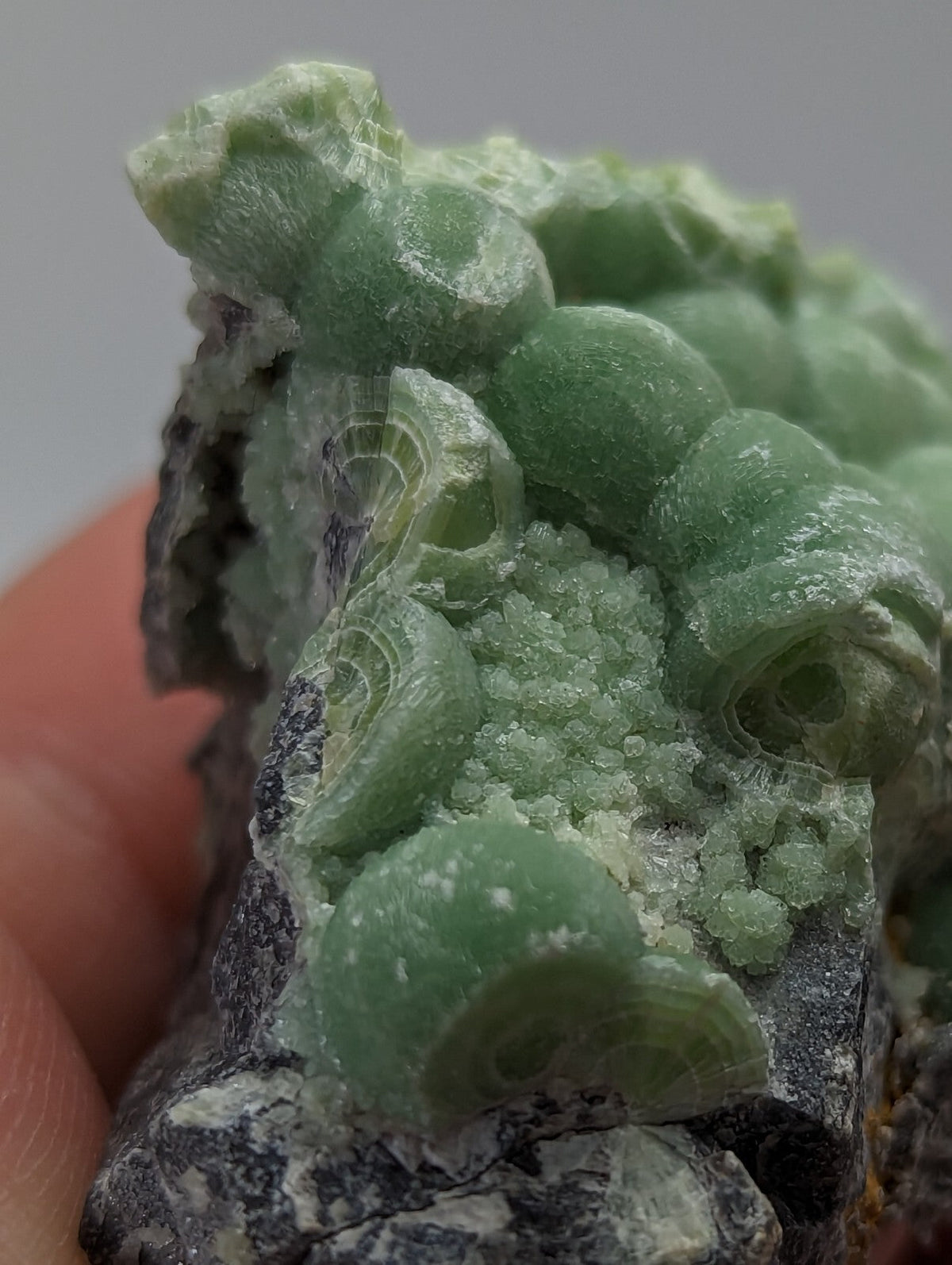 A cluster of translucent green calcite crystals with rounded, layered formations growing from a dark gray rock base.