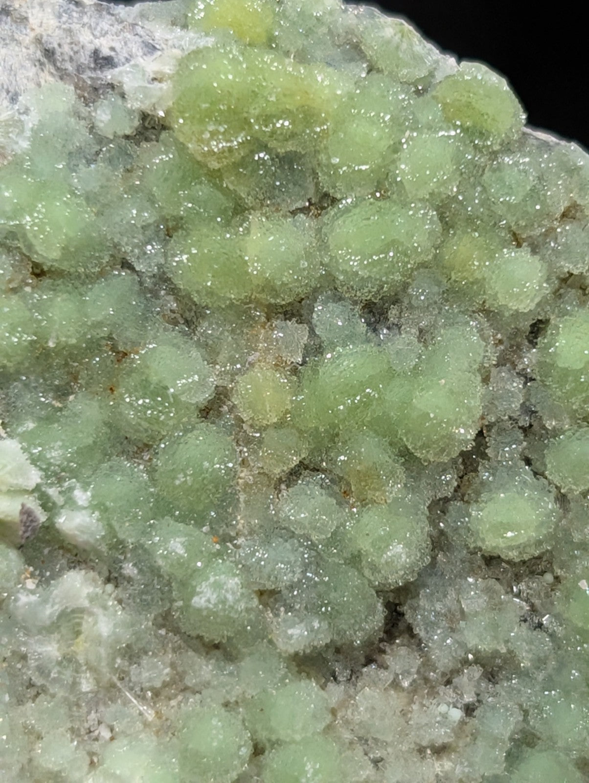 A cluster of translucent, light green crystalline formations with a slightly rough and textured surface.