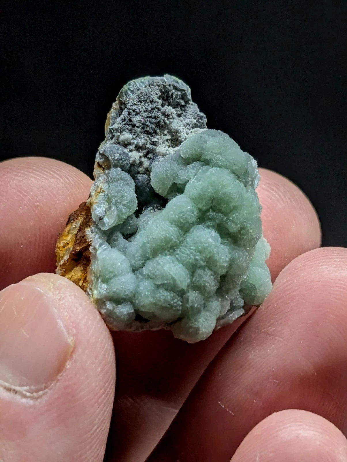 A delicate, light green mineral specimen with a textured, clustered formation and grayish matrix.