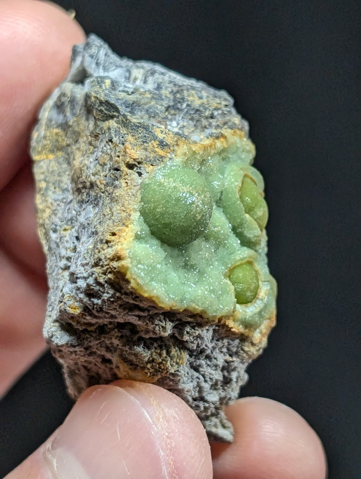 A rough, gray rock with a vibrant green mineral formation featuring rounded, glossy spheres embedded in its surface.