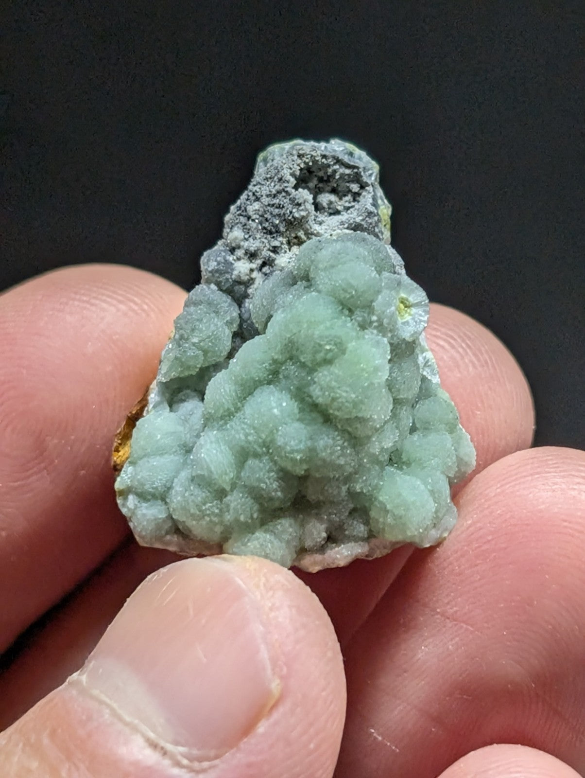 A light green, bumpy mineral specimen with a rough, crystalline texture and some grayish patches.